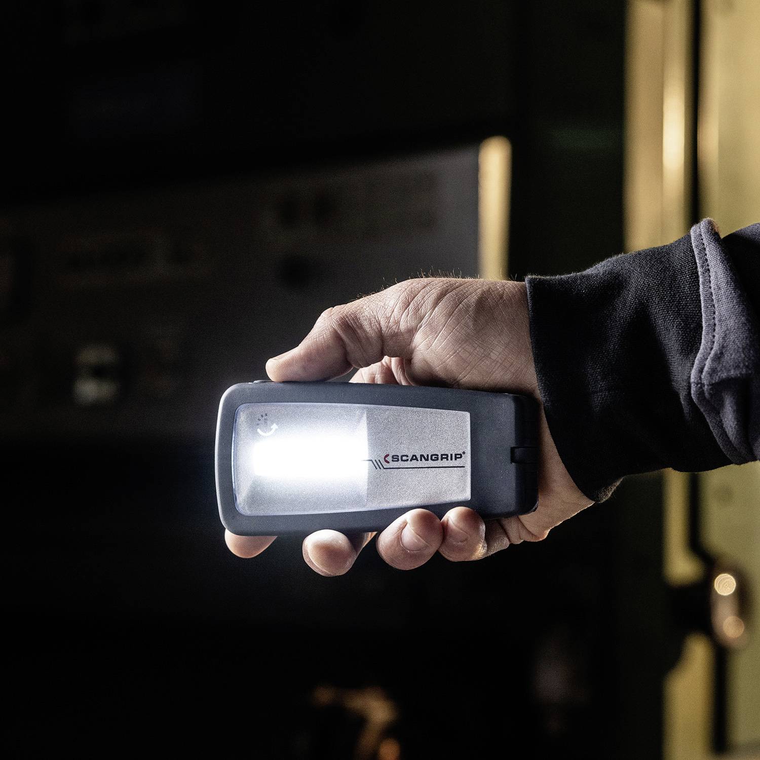 Eine Person hält eine tragbare Arbeitsleuchte in der Hand, die im Dunkeln leuchtet. Ihre Hand ist in einem schwarzen Ärmel gekleidet.