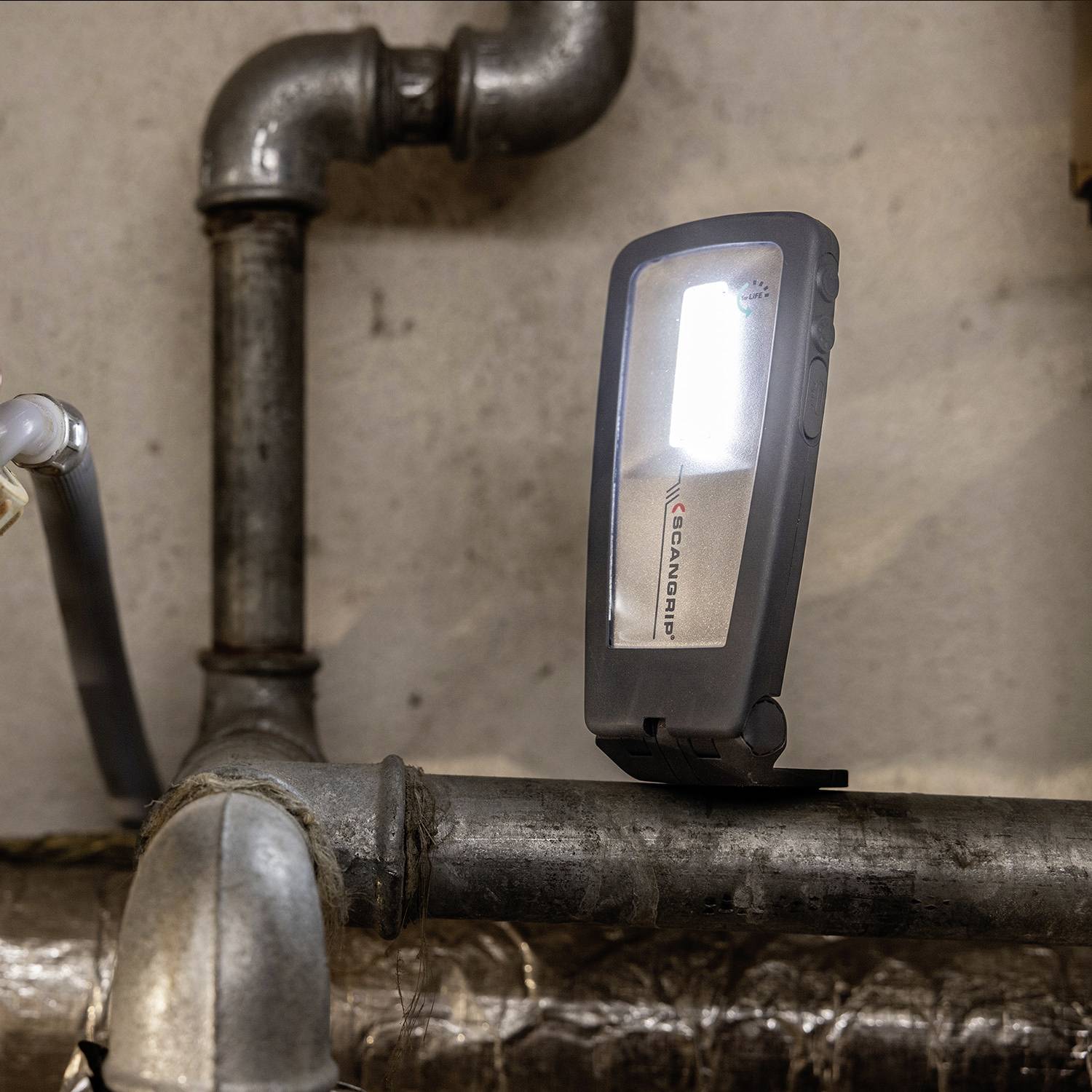 Eine kleine tragbare Lampe leuchtet ein graues Rohr in einem Keller oder Arbeitsraum aus.