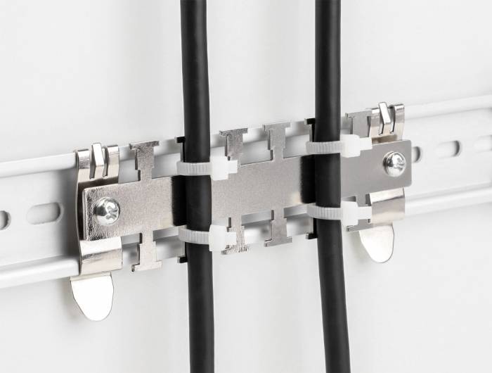 Zwei schwarze Kabel sind mit Metallklemmen an einer weißen Schiene befestigt. Die Klemmen halten die Kabel ordentlich in Position.