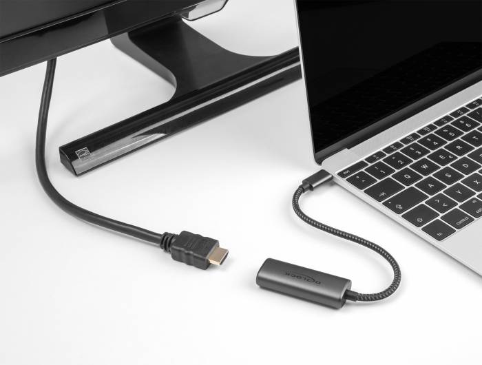 Ein Adapter verbindet einen Laptop mit einem externen Monitor über ein HDMI-Kabel. Der Laptop und der Monitor sind beide schwarz.