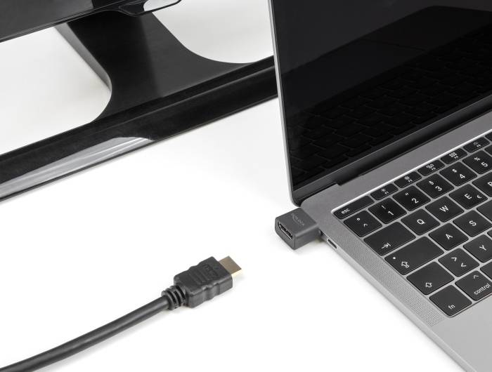 Ein HDMI-Kabel liegt neben einem Laptop und einem Monitorständer. Der Laptop hat einen Adapter im USB-C-Port, der HDMI unterstützt.