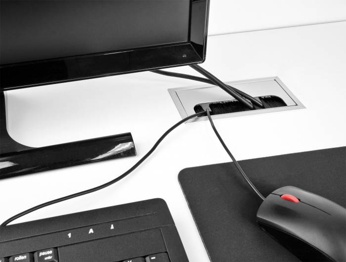Monitor, Tastatur und Maus auf einem Schreibtisch, verbunden durch Kabel. Die Kabel verlaufen durch eine Öffnung in der Tischoberfläche.