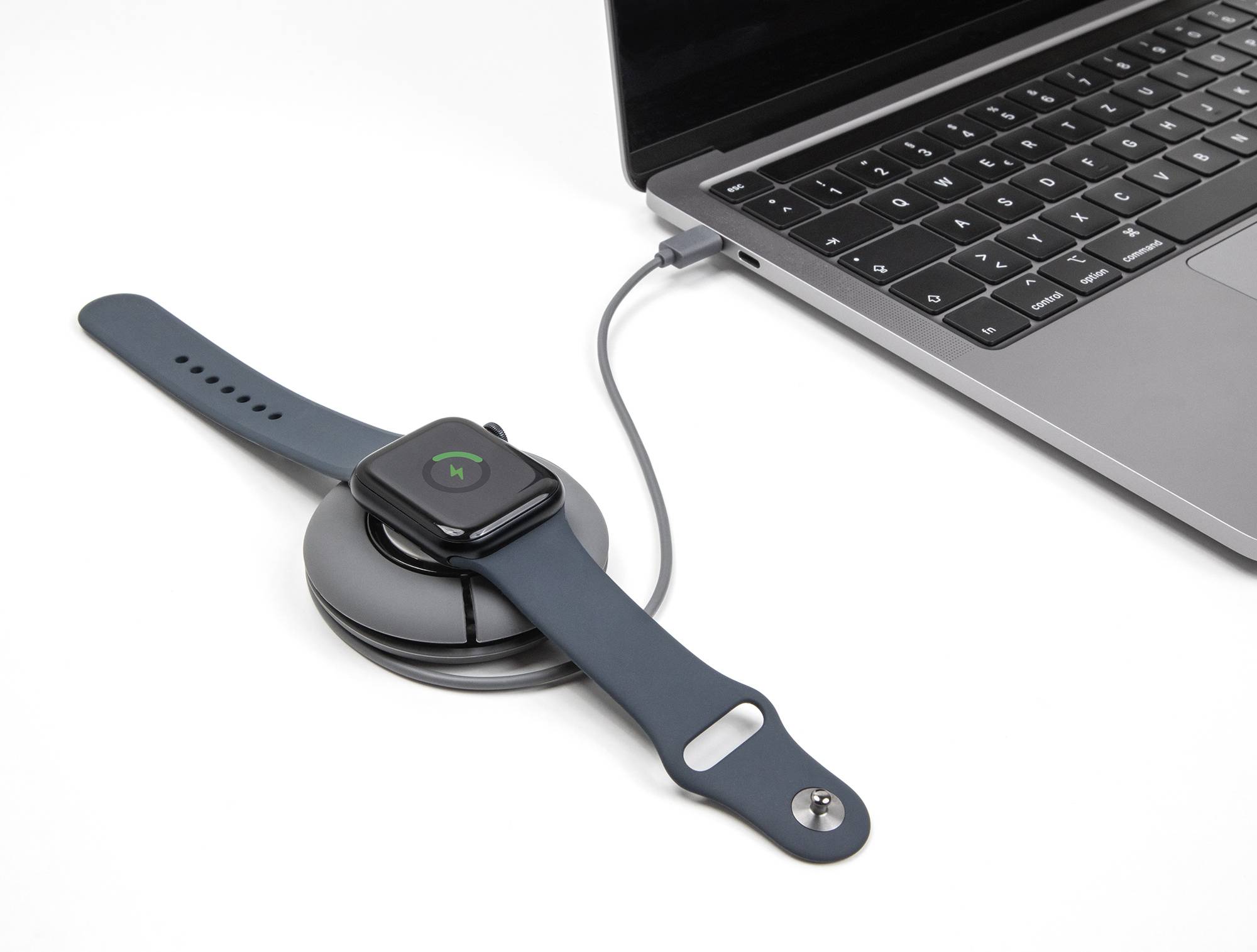 Eine Smartwatch wird mit einem USB-Kabel an einem Laptop aufgeladen. Die Uhr zeigt ein Ladesymbol auf dem Bildschirm.