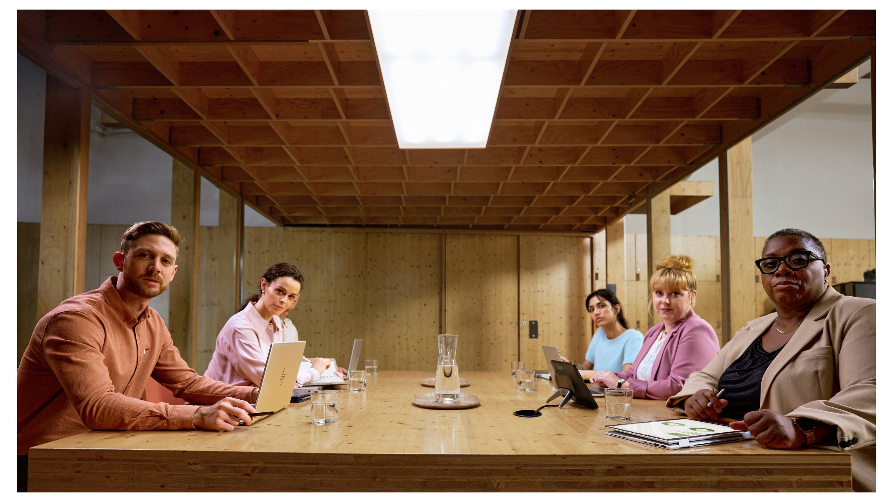 Sechs Personen an einem Konferenztisch in moderner Holzausstattung, mit Laptops vor sich, in einem Besprechungsraum.