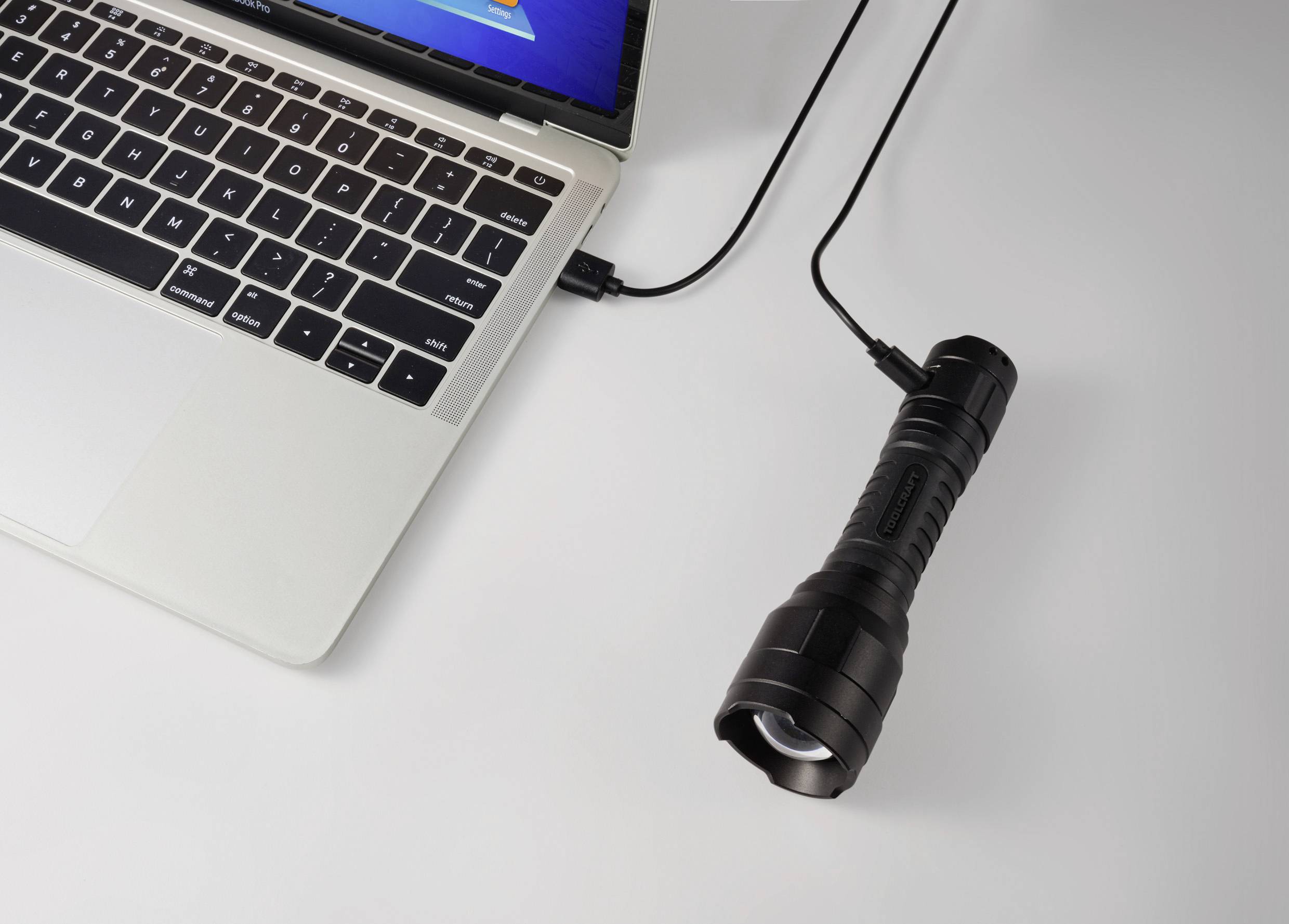Ein Laptop verbunden mit einer Taschenlampe über ein USB-Kabel auf einem Tisch.