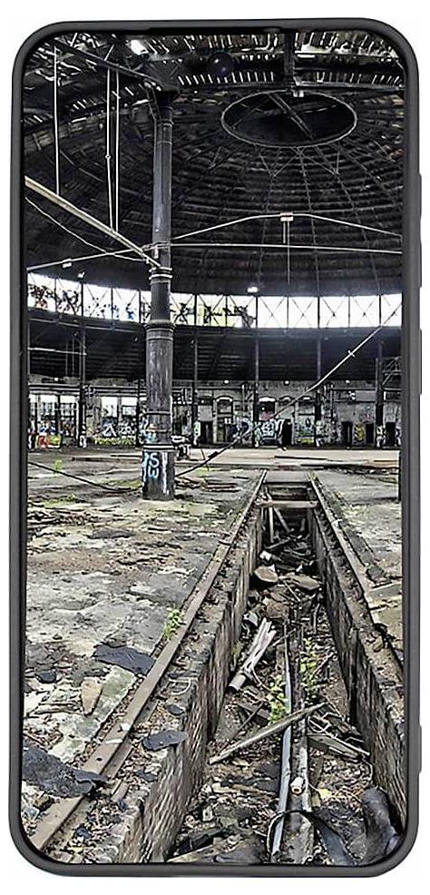 Alter, verlassener Industriebereich in einer großen, leeren Halle mit Schienen, Schmutz und Graffiti auf den Säulen.