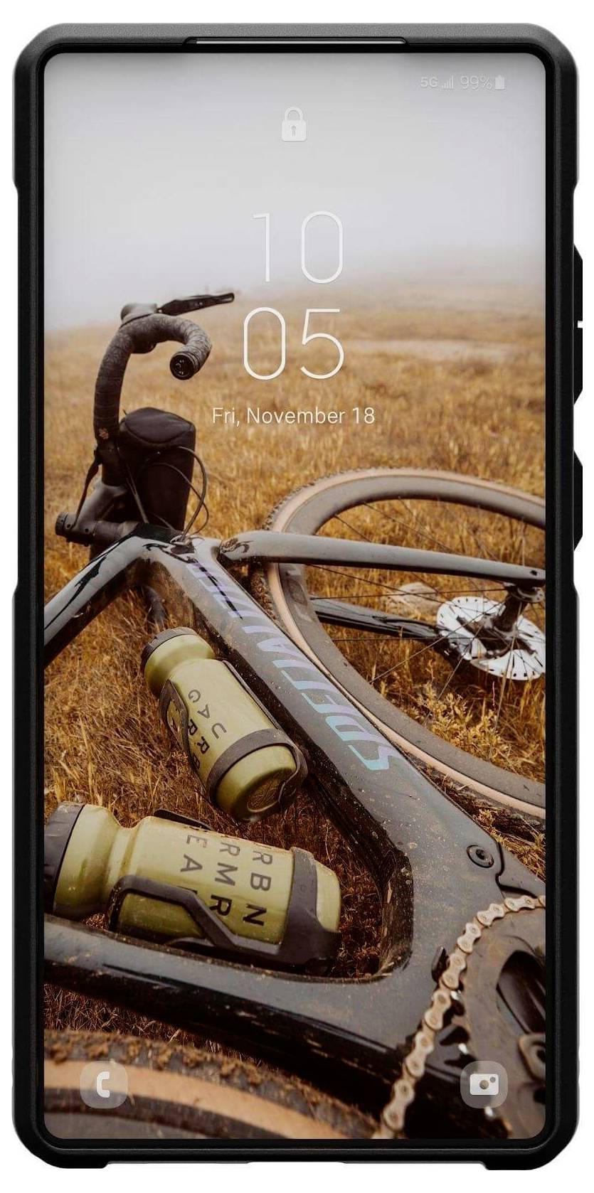 Ein Fahrrad liegt auf einem grasbewachsenen Hügel. Der Smartphone-Bildschirminhalt zeigt Uhrzeit und Datum ('10:05, Fr, 18. November').