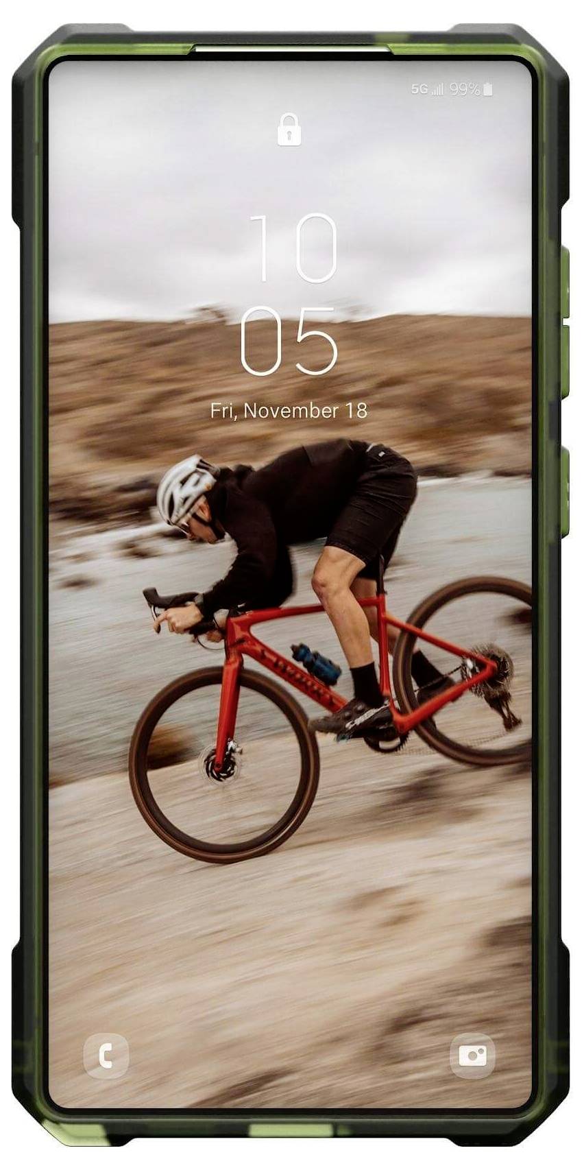 Ein Radfahrer mit Helm fährt auf einem roten Fahrrad schnell einen Sandweg entlang. Hintergrund zeigt felsige Landschaft und Wasser.