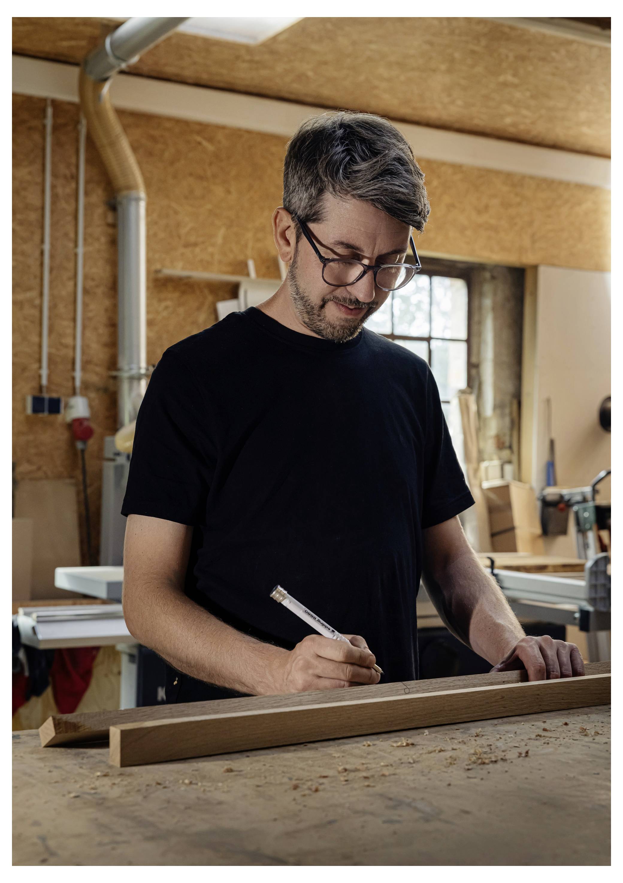 Mann in einer Werkstatt, der ein Holzbrett auf einer Werkbank misst und markiert, konzentriert sich auf Zimmerei oder Holzbearbeitung.