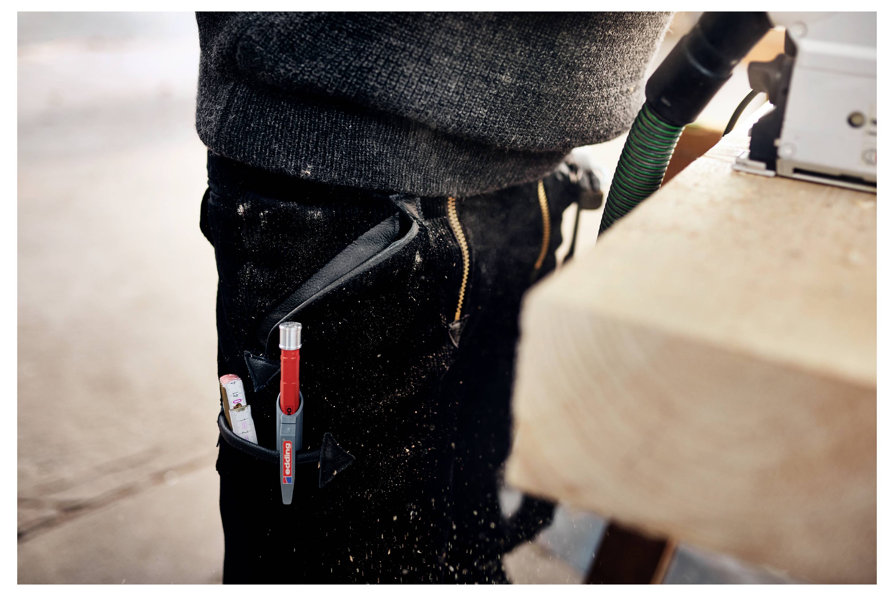 Nahaufnahme der Taille eines Arbeiters mit Stift und Universalmesser in einer Gürteltasche neben einer Säge, die Holz schneidet.