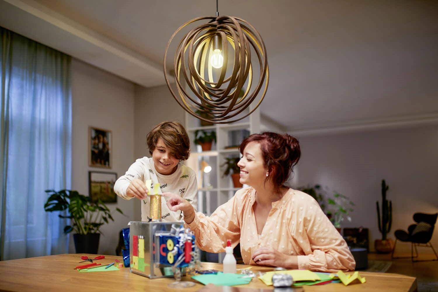 Ein Kind und eine Frau basteln zusammen an einem Tisch, umgeben von Papier und Basteleien. Beide wirken fröhlich und konzentriert.