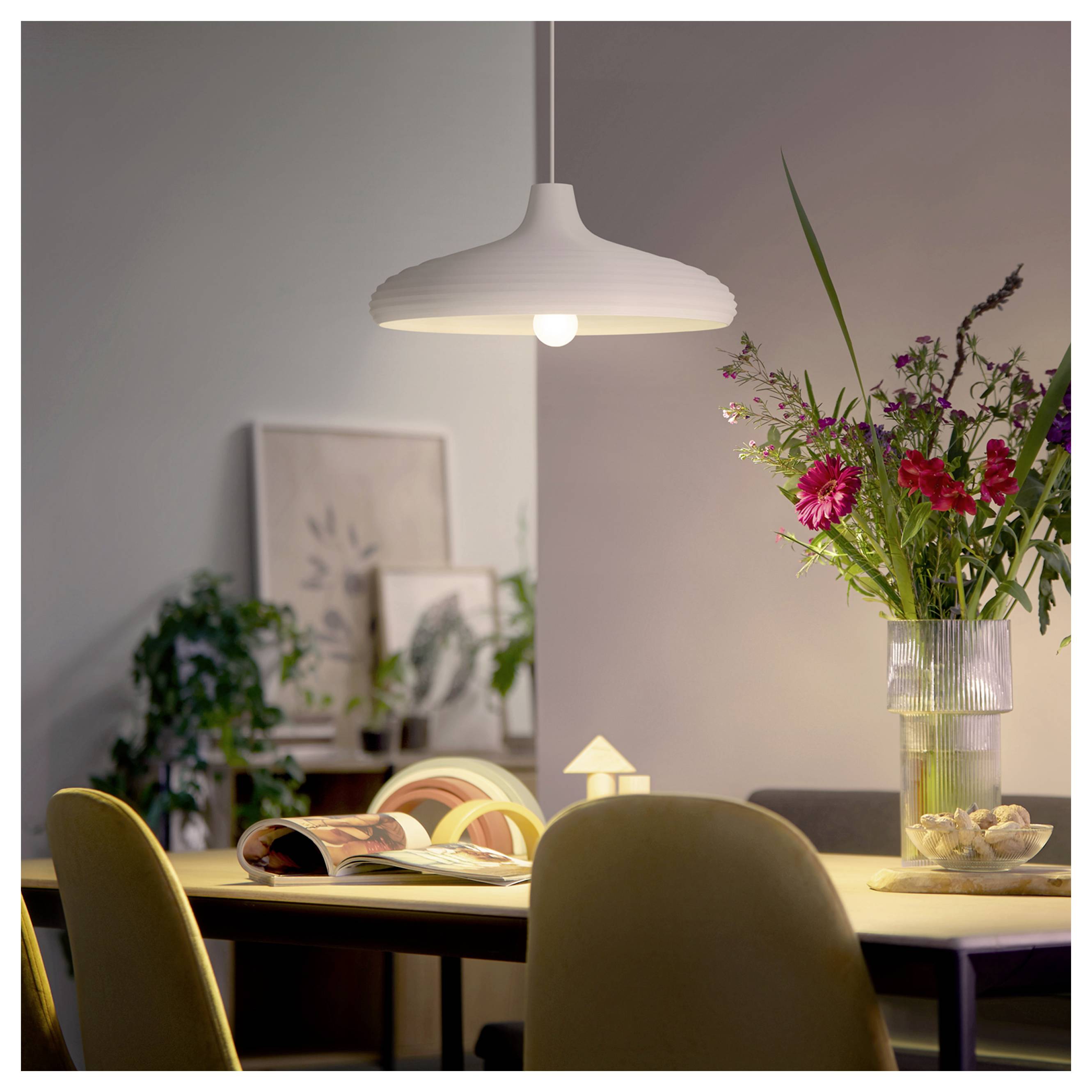 Modernes Esszimmer mit einer weißen Pendelleuchte über einem Tisch, der mit einem aufgeschlagenen Buch und einer Blumenvase eingedeckt ist.