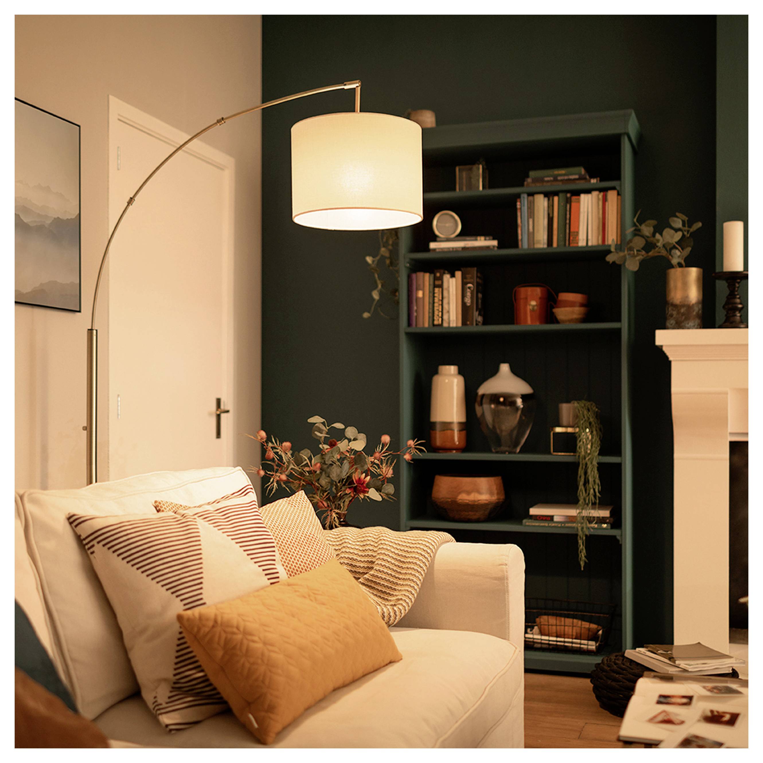 Gemütliches Wohnzimmer mit weißem Sofa, gemusterten Kissen, Stehleuchte, dunkelem Bücherregal und Kaminsims.