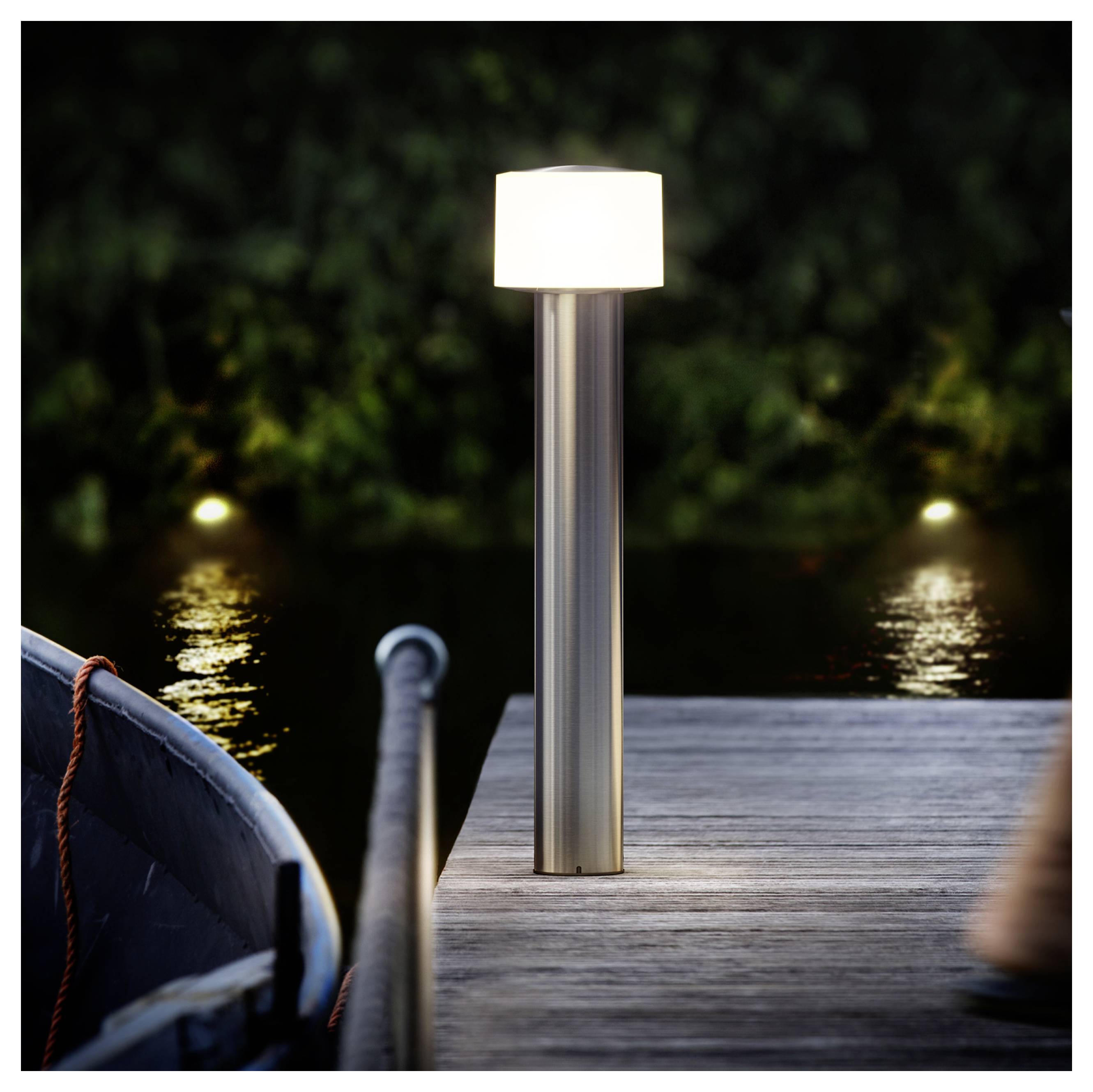Moderne Außenleuchte, die auf einem Holzsteg neben ruhigem Wasser in der Nacht leuchtet, mit einem teilweise sichtbaren Boot auf der linken Seite.