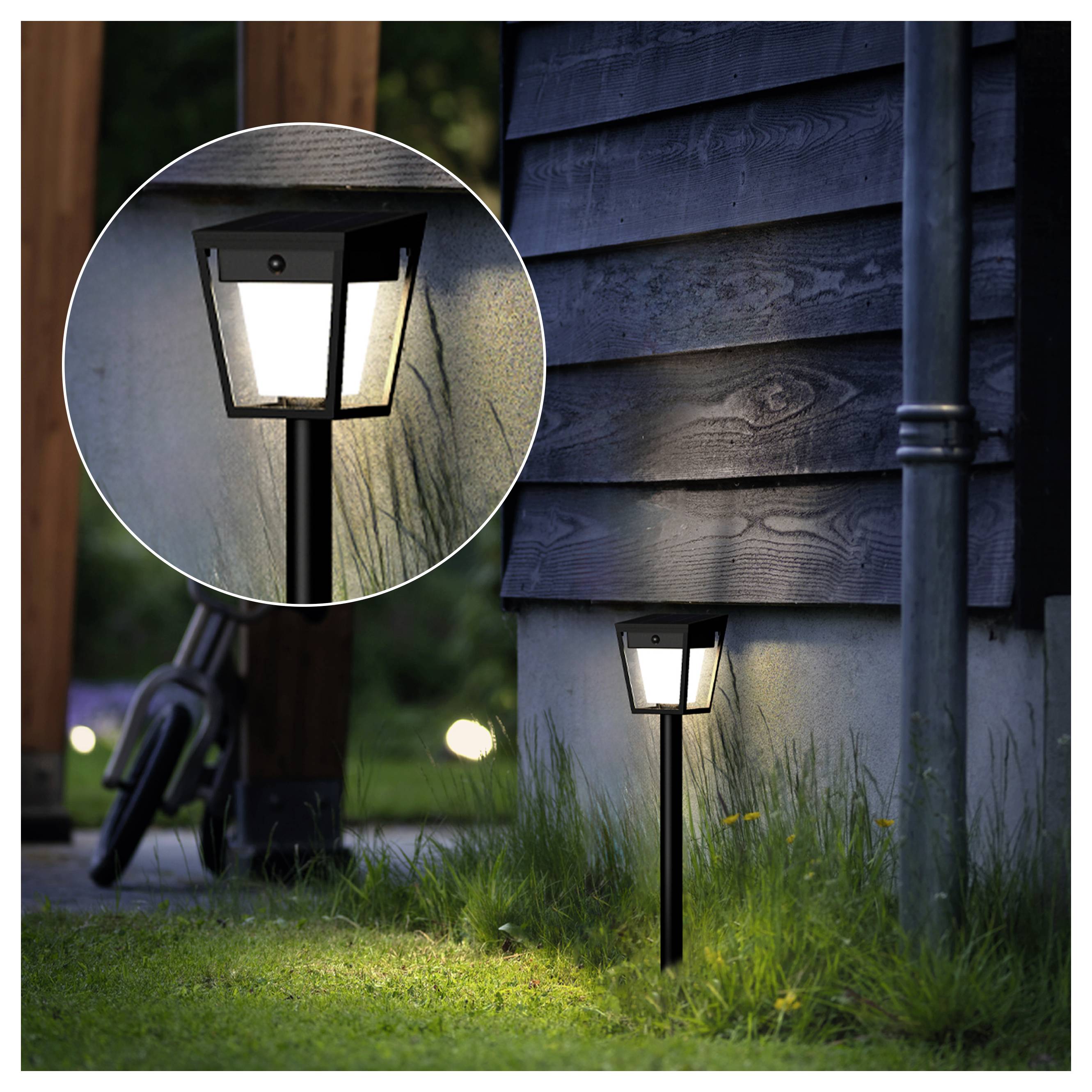 Kleine Außenwegleuchte, die neben einer Hauswand leuchtet, mit einer kreisförmigen Vergrößerung, die eine Nahaufnahme der Lampe zeigt.