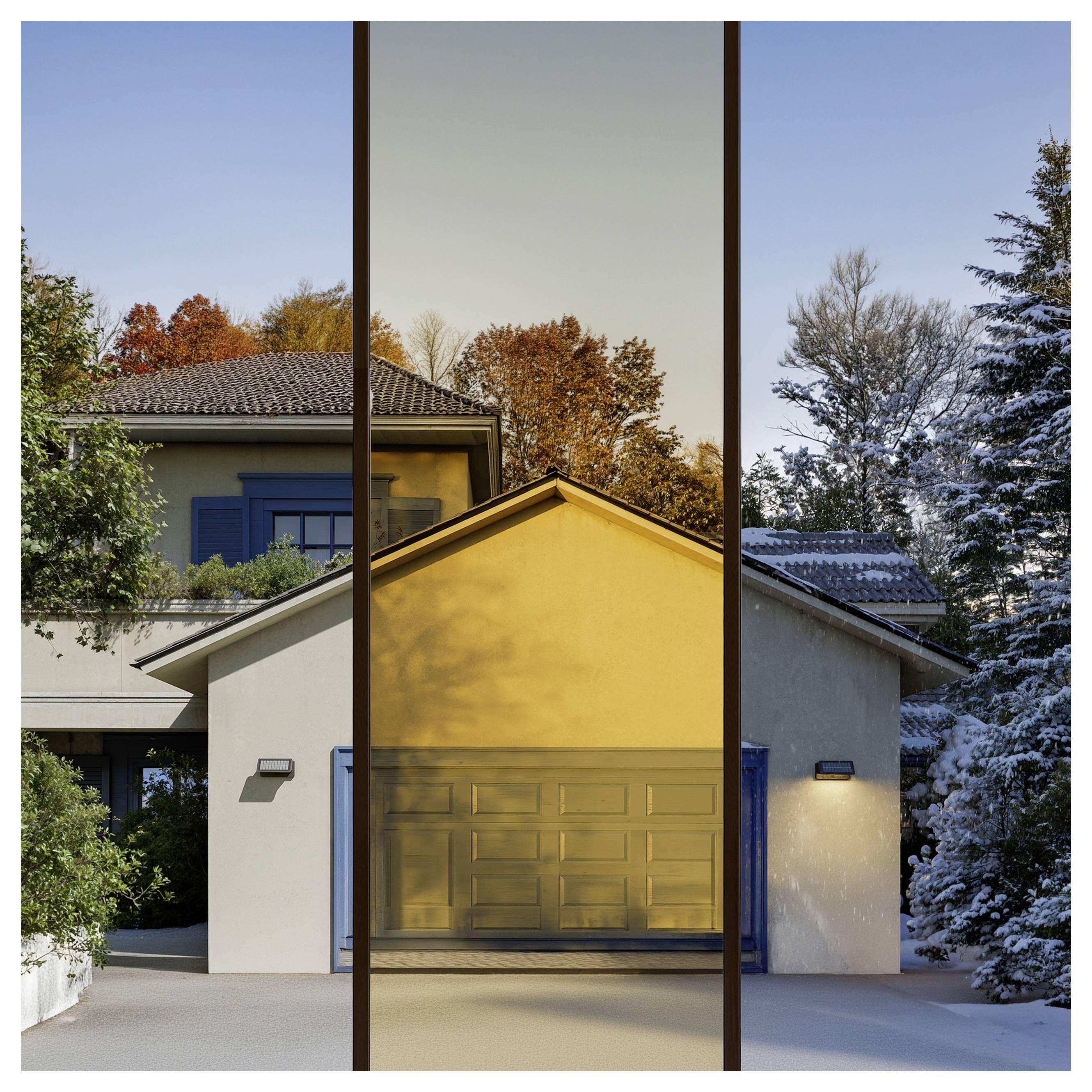 Moderne Hausfront mit blauer Garagentür, weißen Wänden und hohen Glaspaneelen, die Herbstbäume und einen verschneiten Hof spiegeln.