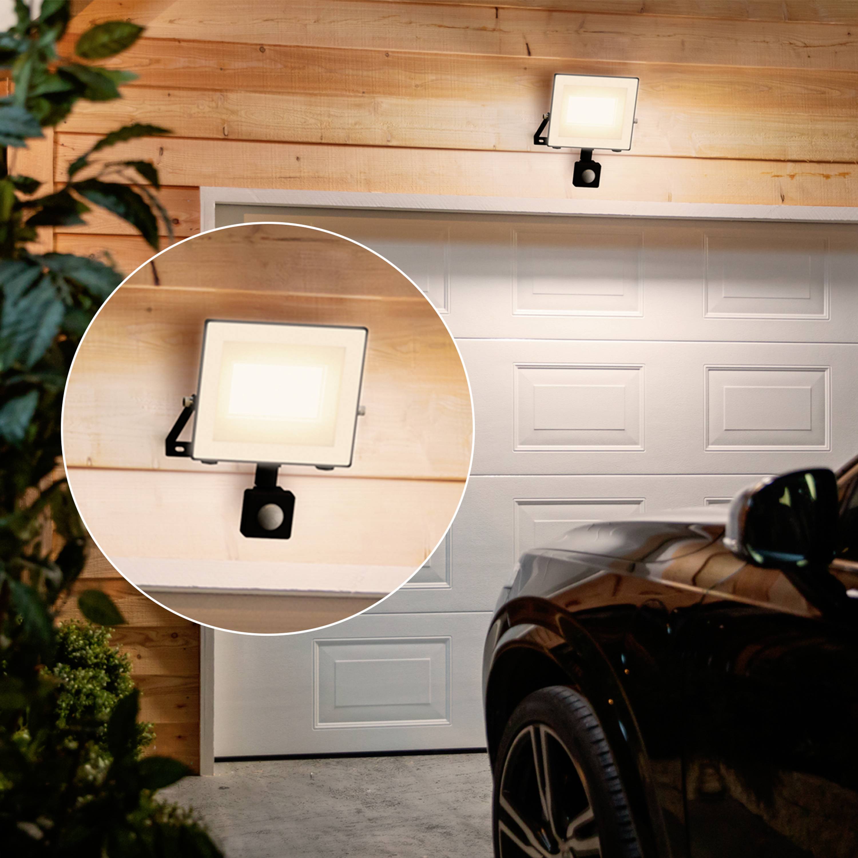 Scheinwerfer beleuchtet Garage über einem weißen Tor, Auto im Vordergrund. Vergrößerter Ausschnitt zeigt Detail des Lichts.