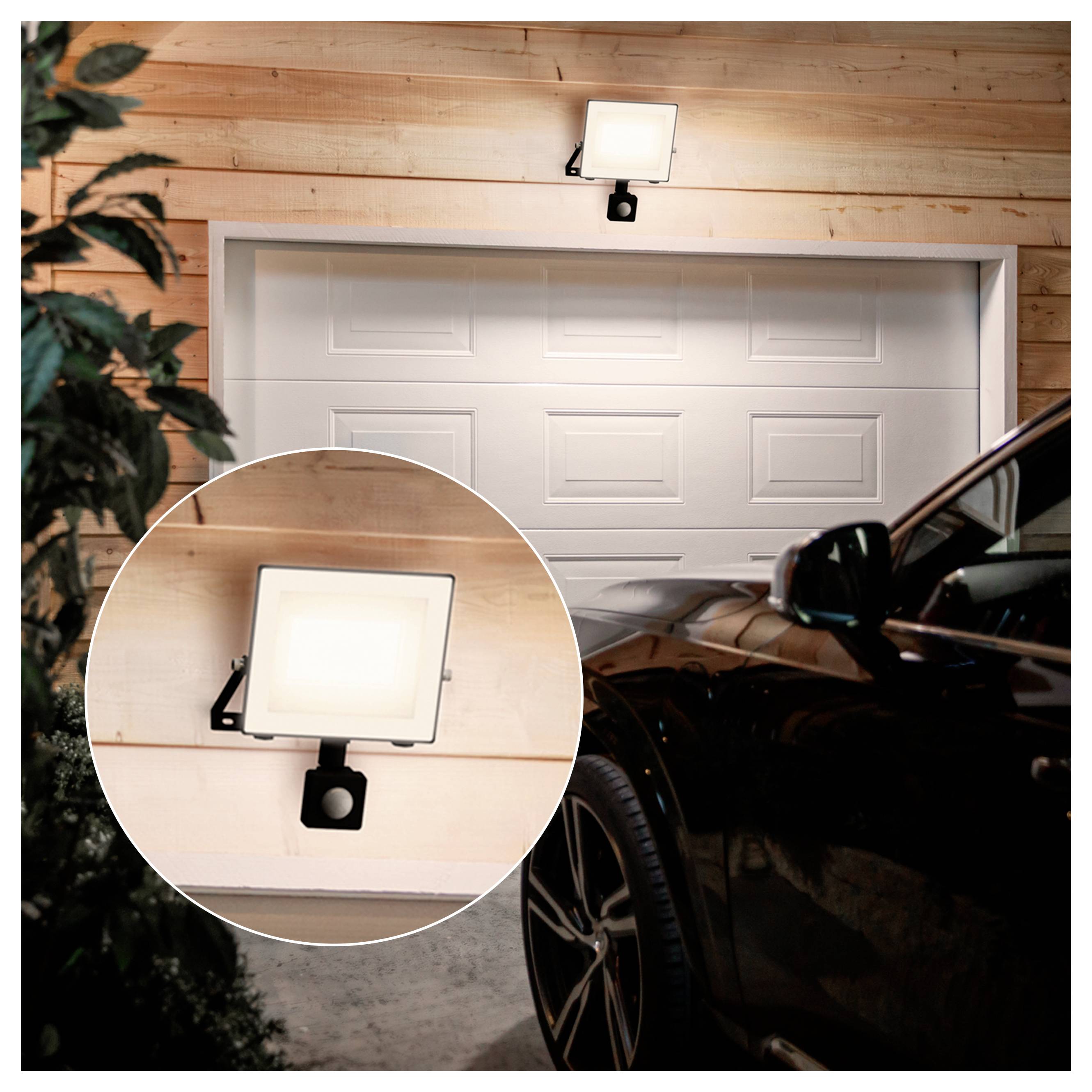 Schwarzes Auto geparkt neben einer Garage mit einer wandmontierten Bewegungsmelder-Flutlichtleuchte über der Tür, dargestellt mit einer kreisförmigen Nahaufnahme des Lichts.