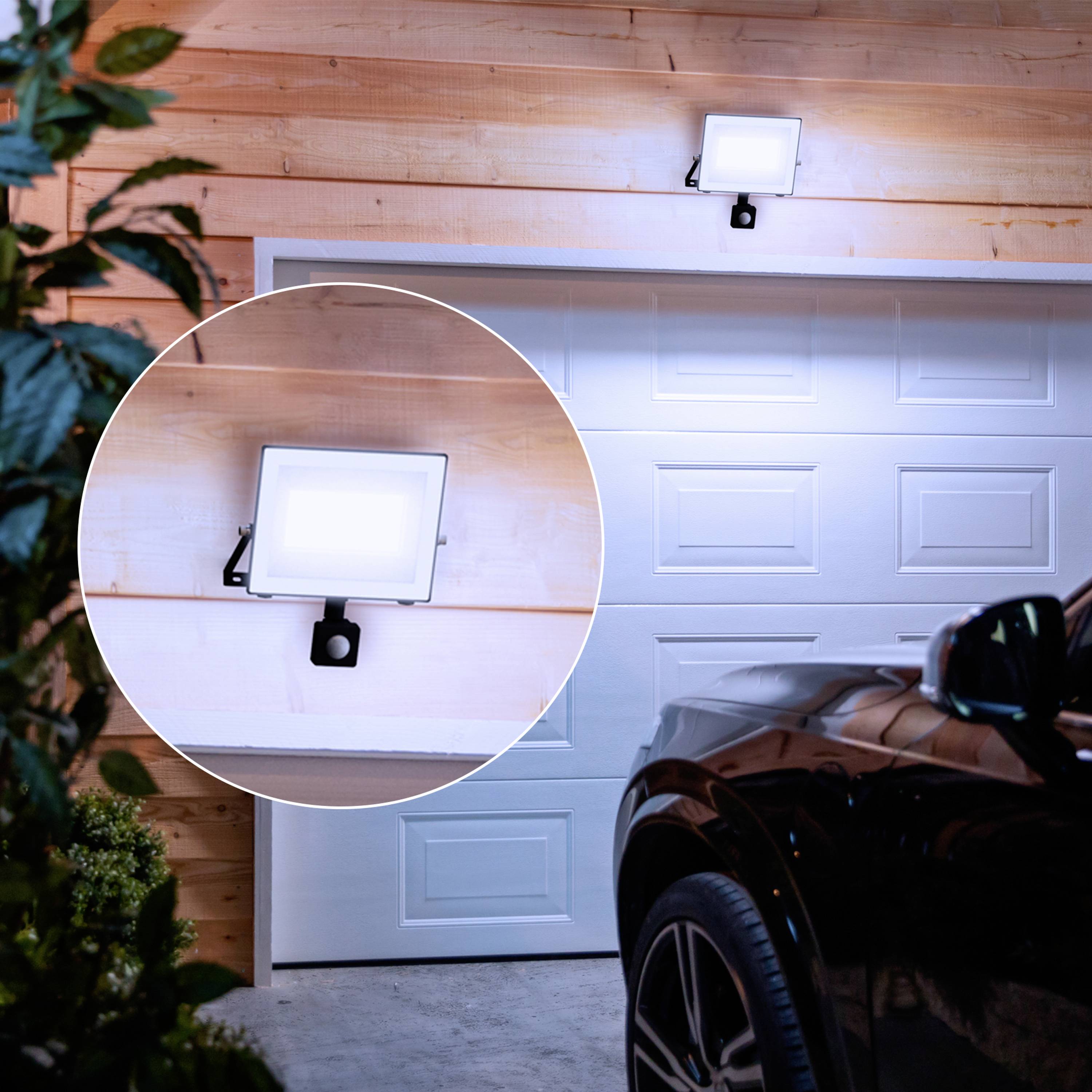 Außenleuchte beleuchtet automatisch eine Garage bei Einbruch der Dunkelheit; Auto vor der Garage geparkt.