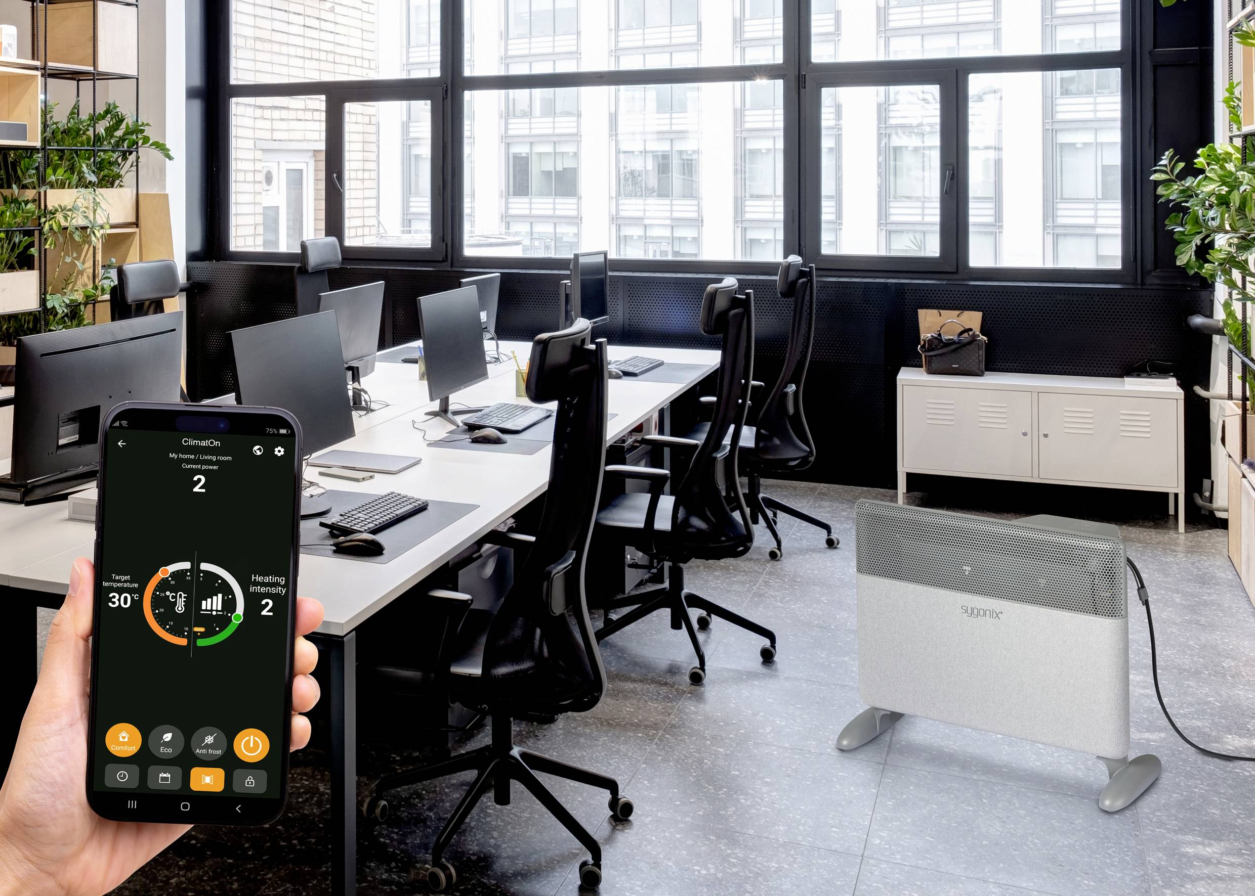 Ein Smartphone steuert einen elektrischen Heizkörper in einem modernen Büro mit offenem Grundriss. Auf dem Bildschirm sind Heizregelungen zu sehen.