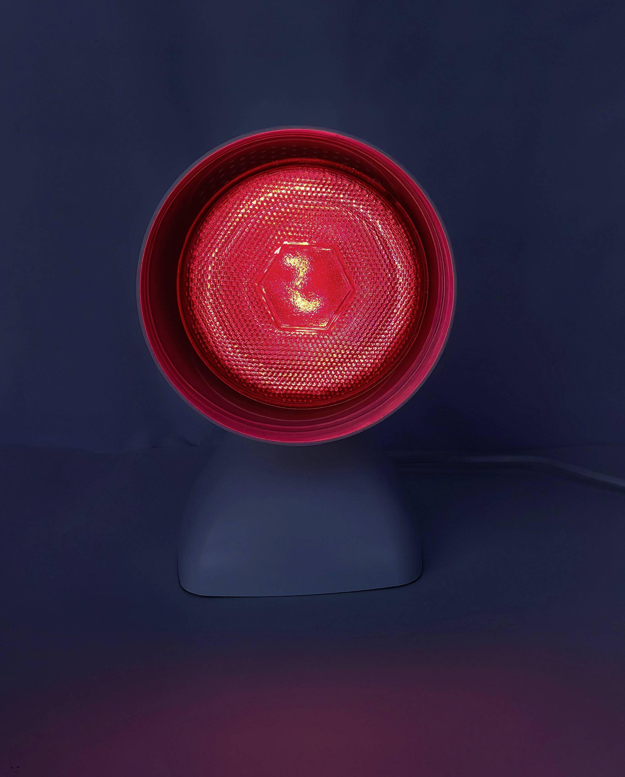 Eine rote Infrarotlampe mit kreisförmigem Design auf dunklem Hintergrund, die ein warmes Leuchten ausstrahlt und häufig zu therapeutischen Zwecken eingesetzt wird.