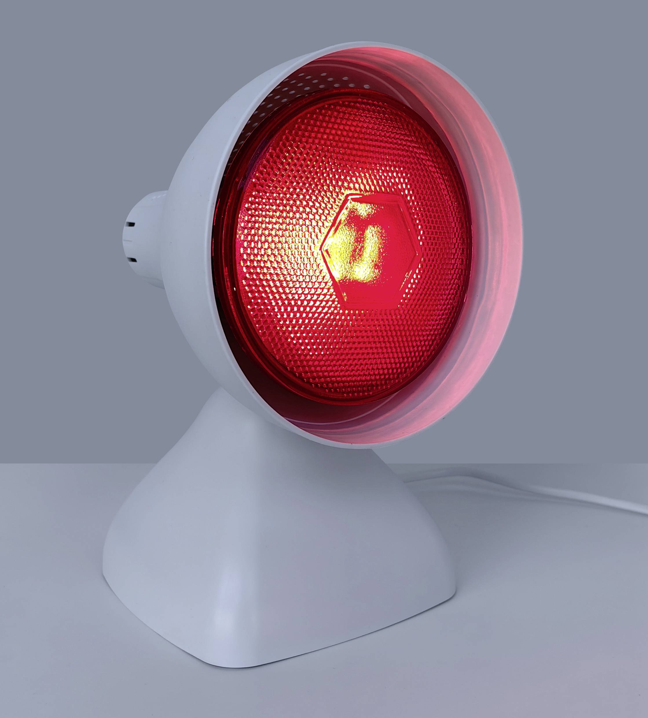 Eine weiße Infrarot-Wärmelampe mit einem glühend roten Licht, die auf einer grauen Oberfläche platziert ist und zu therapeutischen Zwecken verwendet wird.