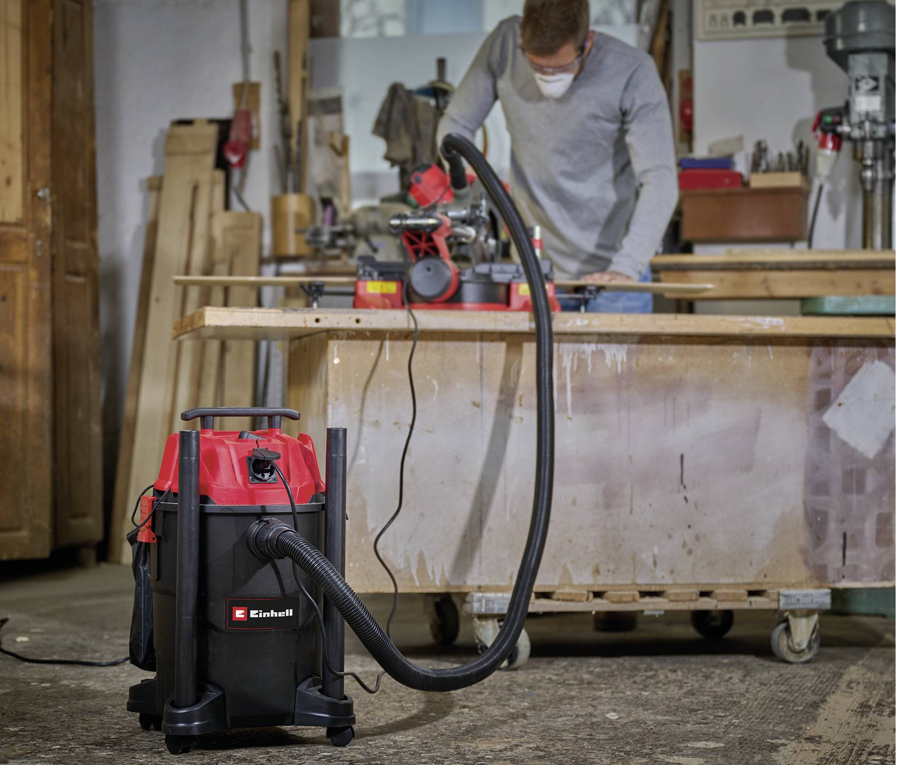 Eine Person arbeitet in einer Werkstatt an einem Tisch mit einem elektrischen Schleifgerät. Im Vordergrund steht ein Industriestaubsauger.