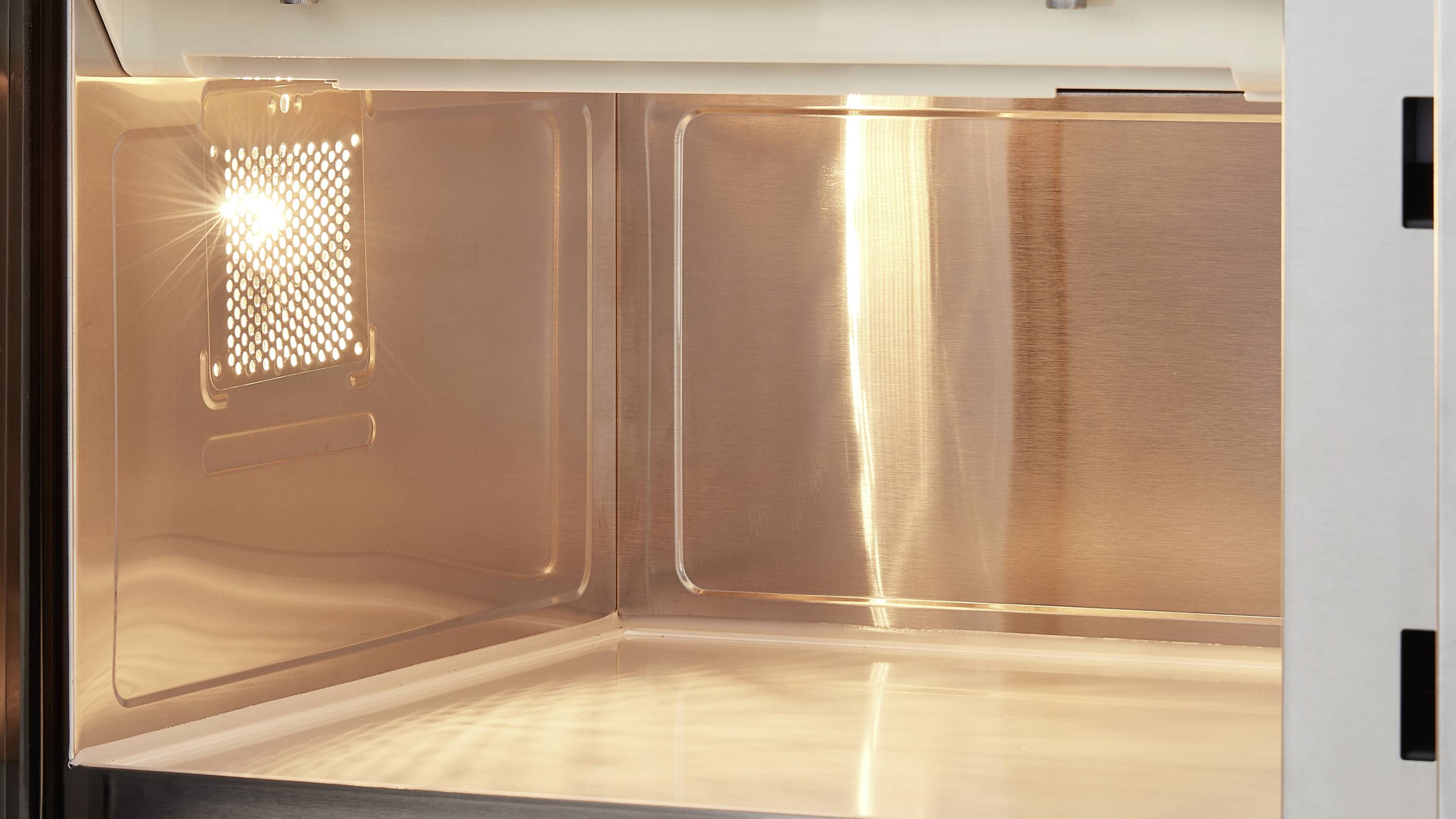 Offene Mikrowelle mit leuchtendem Innenraum, die saubere und glänzende Metalloberfläche zeigt.