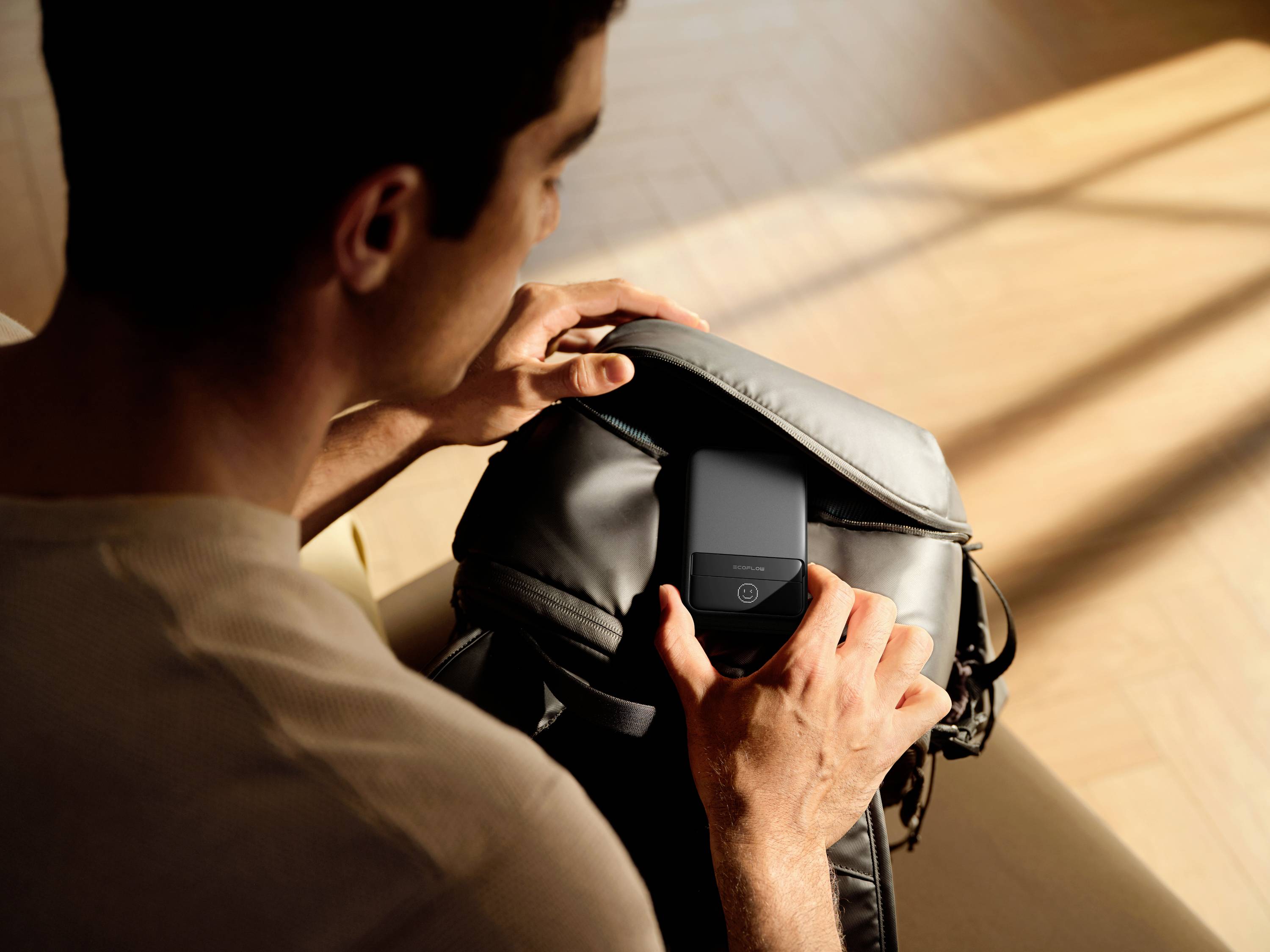 Eine Person öffnet einen Rucksack, um ein Smartphone herauszunehmen. Das Licht im Raum ist warm und weich.