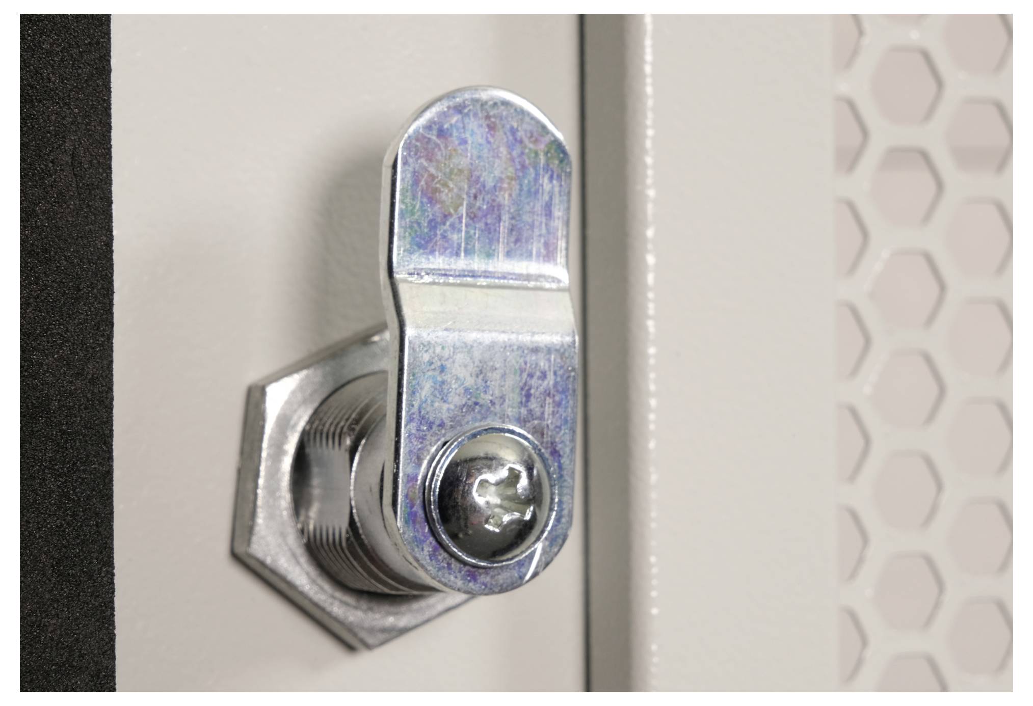 Nahaufnahme eines Metallzylinderschlosses an einer Paneeltür, wobei ein sechseckiges Netzgittermuster im Hintergrund sichtbar ist.