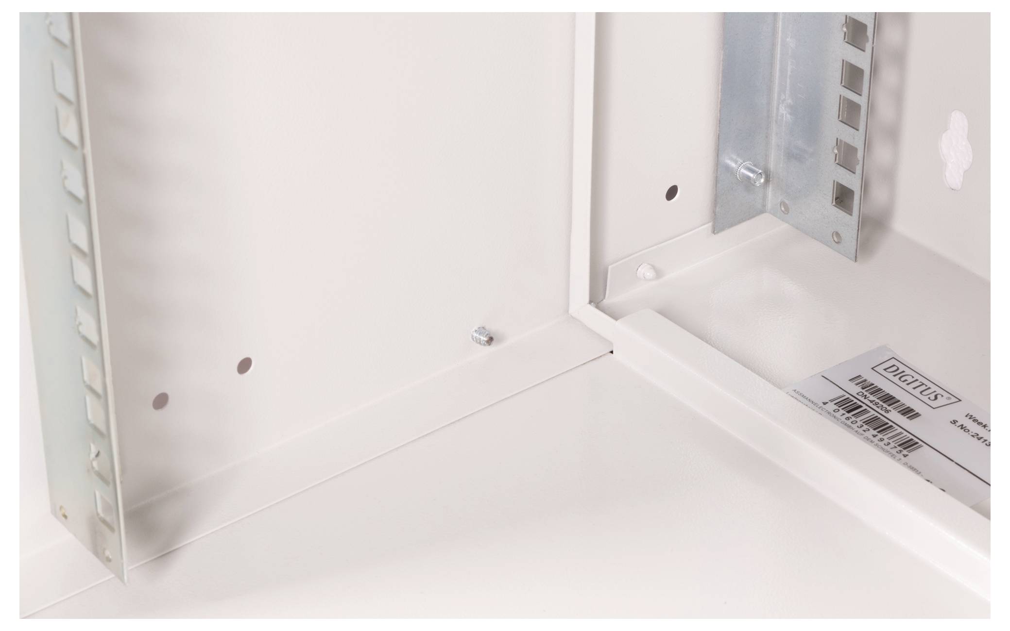 Elektrisches Gehäuse-Eckbereich mit metallischem Rahmen, Lüftungslöchern und einem Dokumentenhalter mit teilweise sichtbarem Etikett.