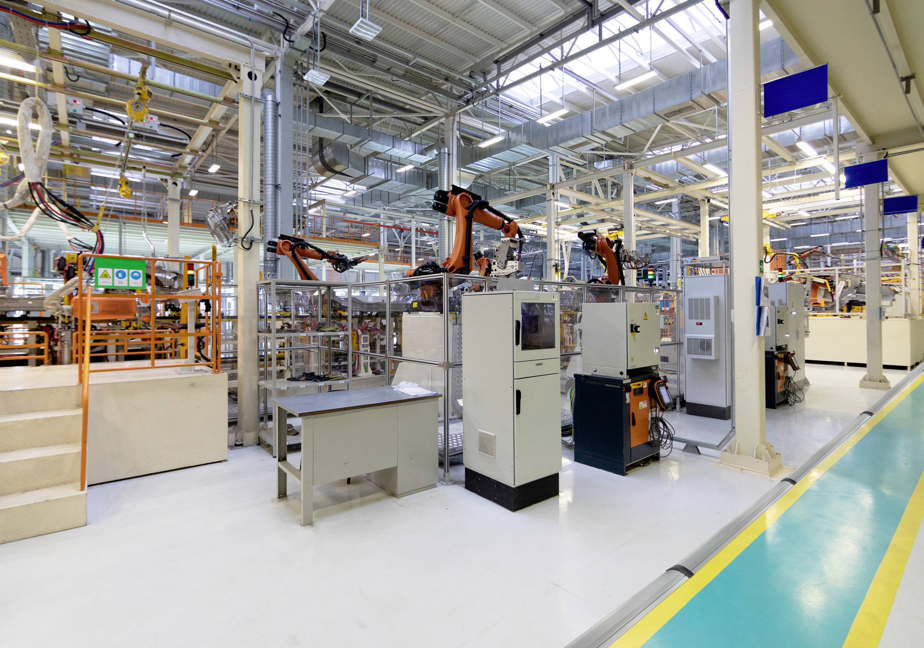 Industrielle Fertigungsanlage mit mehreren Robotern im Einsatz. Hochleuchtende Umgebung mit vielen Maschinen und Kontrollsystemen.