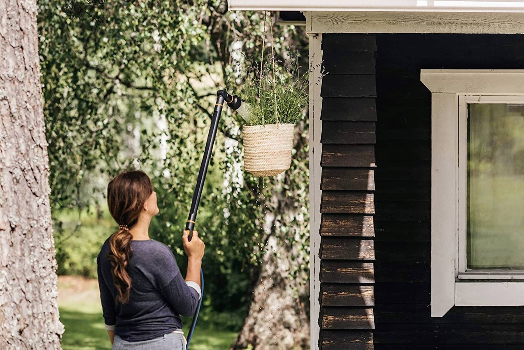Person gießt Pflanzen in einem hängenden Korb an der Hauswand.