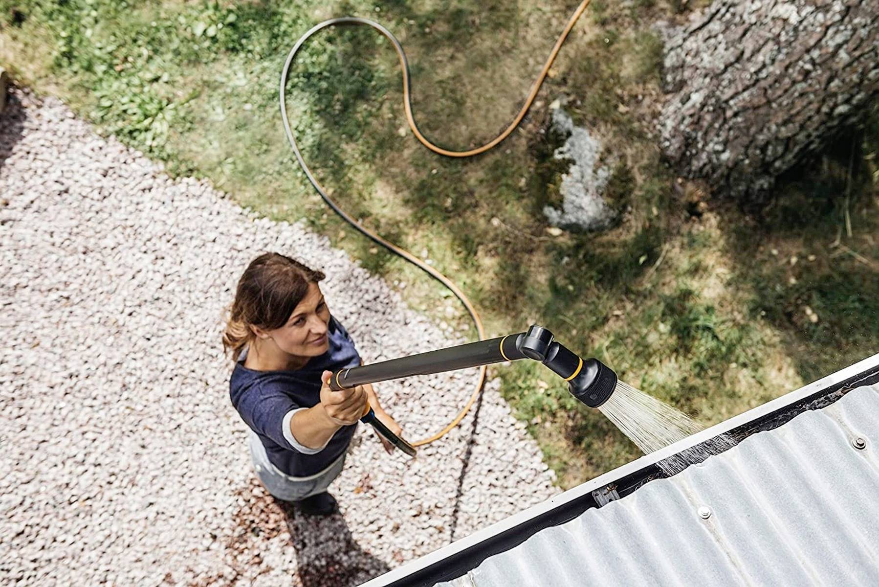Eine Person reinigt eine Dachrinne mit einem Wasserschlauch. Das Bild zeigt die Tätigkeit aus der Vogelperspektive.