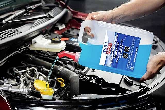 Person füllt Scheibenfrostschutzmittel aus einem Kanister in den Flüssigkeitsbehälter eines Autos ein. Motorhaube ist geöffnet.