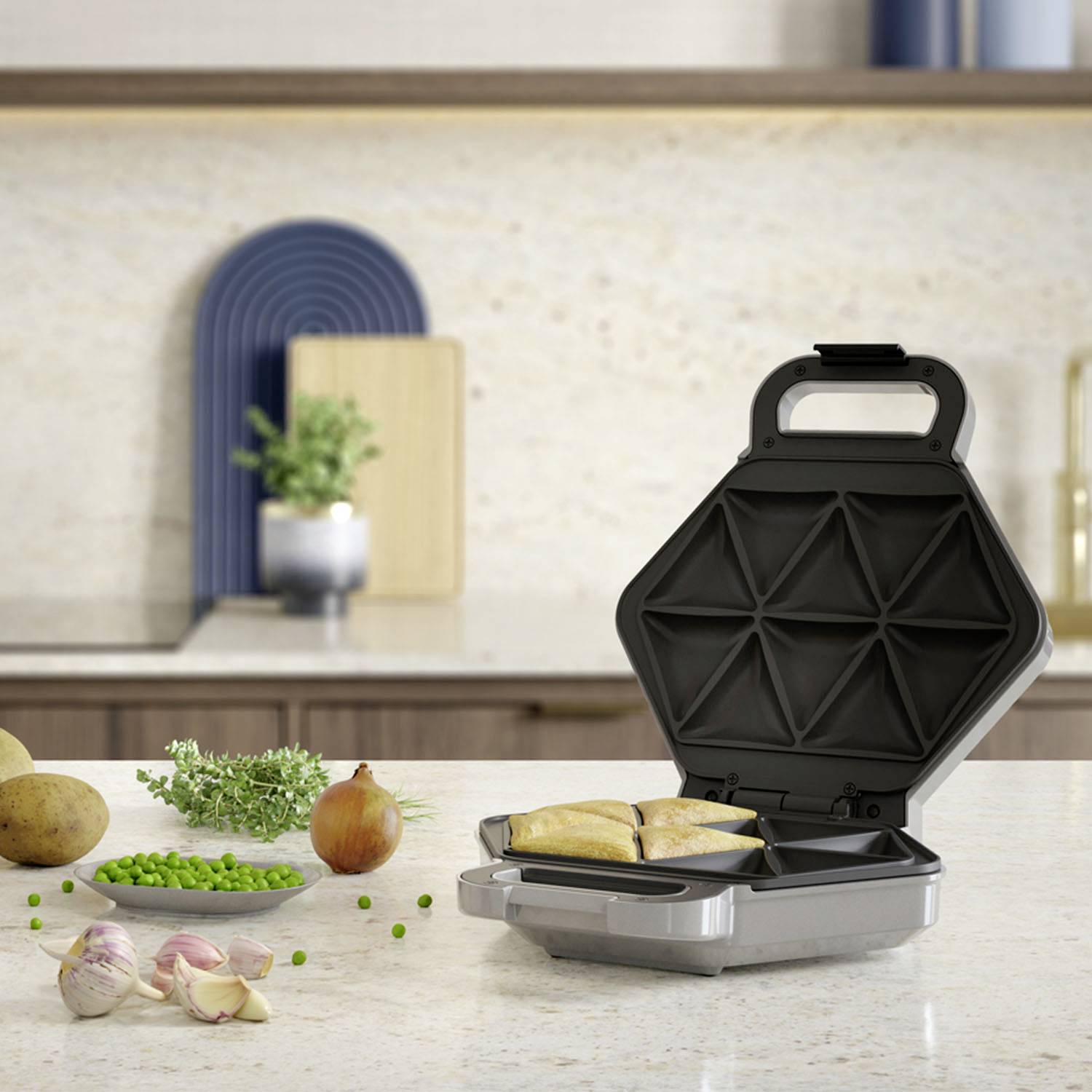 Ein geöffneter Sandwichtoaster steht auf einer Küchenarbeitsplatte mit Zutaten wie Zwiebeln, Kartoffeln und Erbsen im Vordergrund.