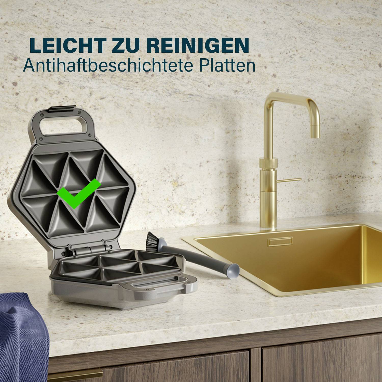 'Leicht zu reinigen' und 'Antihaftbeschichtete Platten' über einem Waffeleisen mit grünem Haken, neben einer Spüle auf der Arbeitsplatte.