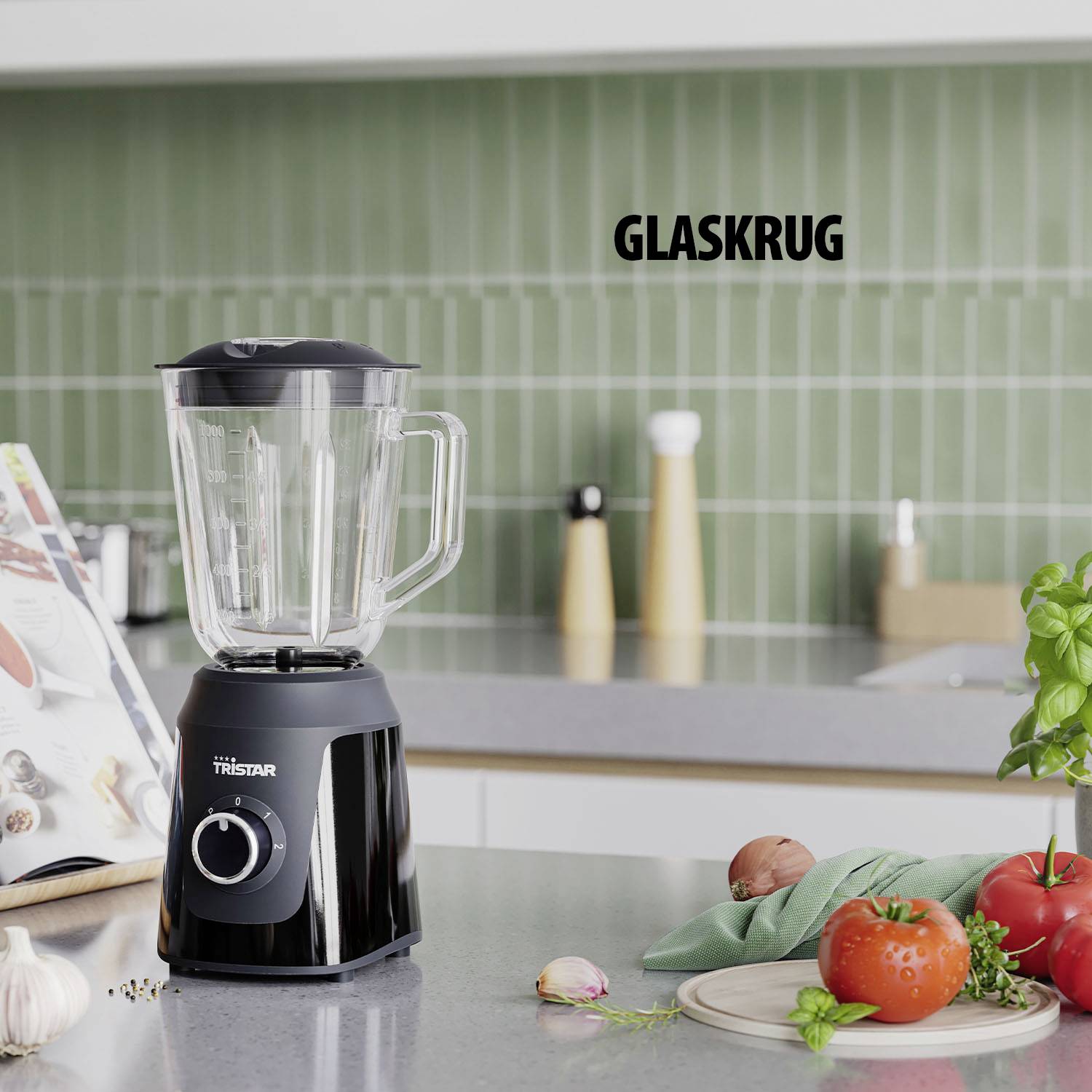 Ein schwarzer Mixer mit Glaskrug steht auf einer Küchenarbeitsplatte. Links sind Kochbücher, im Hintergrund Basilikum und eine Tomate.
