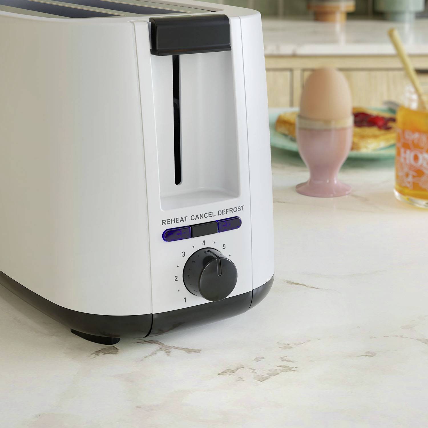 Ein Toaster steht auf einer Küchenarbeitsplatte. Im Hintergrund sind ein weichgekochtes Ei und ein Glas Saft sichtbar.