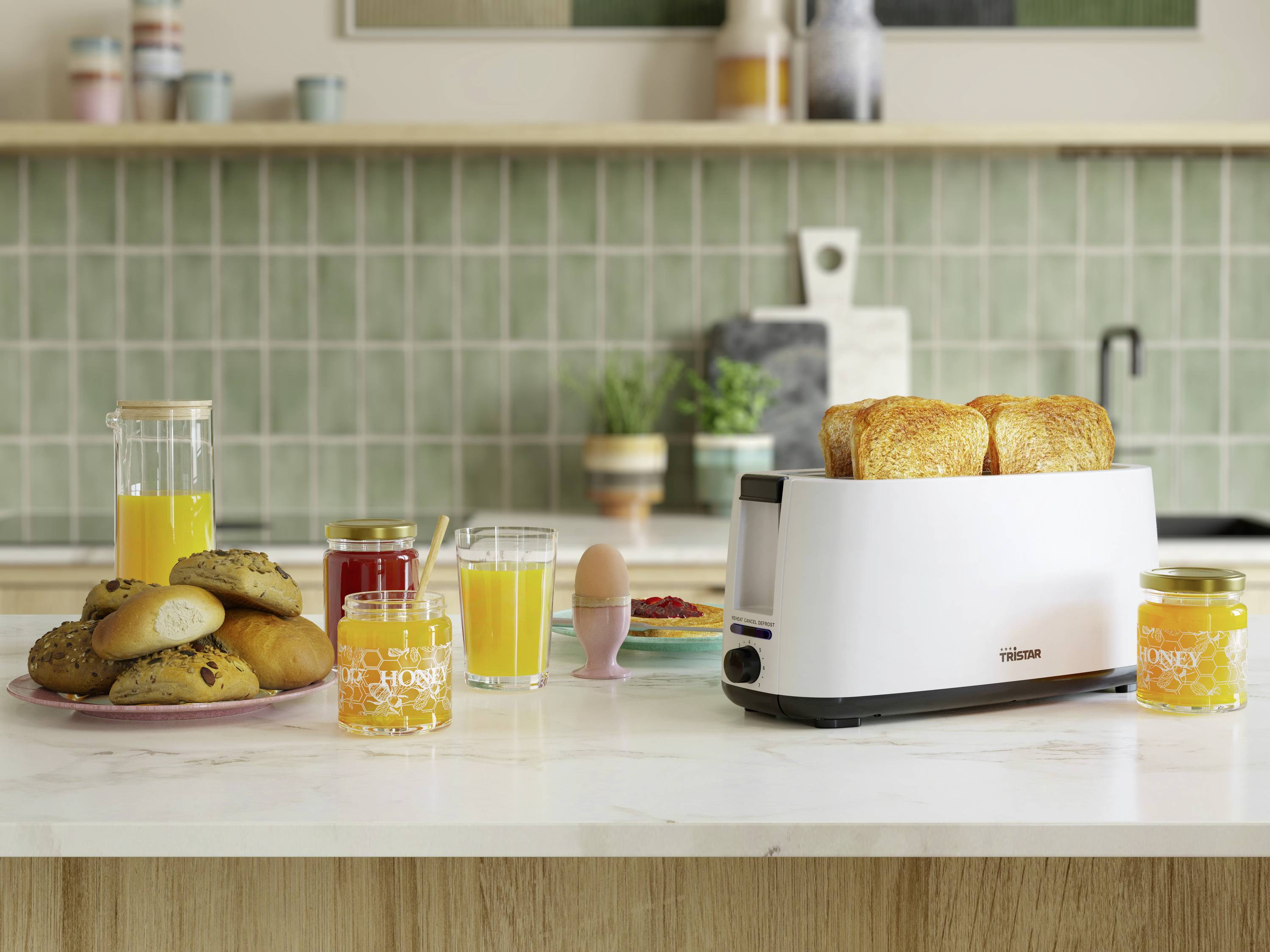 Ein gedeckter Frühstückstisch mit Toaster und Toastscheiben, Saft, Marmelade und Backwaren auf einer Küchenarbeitsplatte vor gefliester Wand.