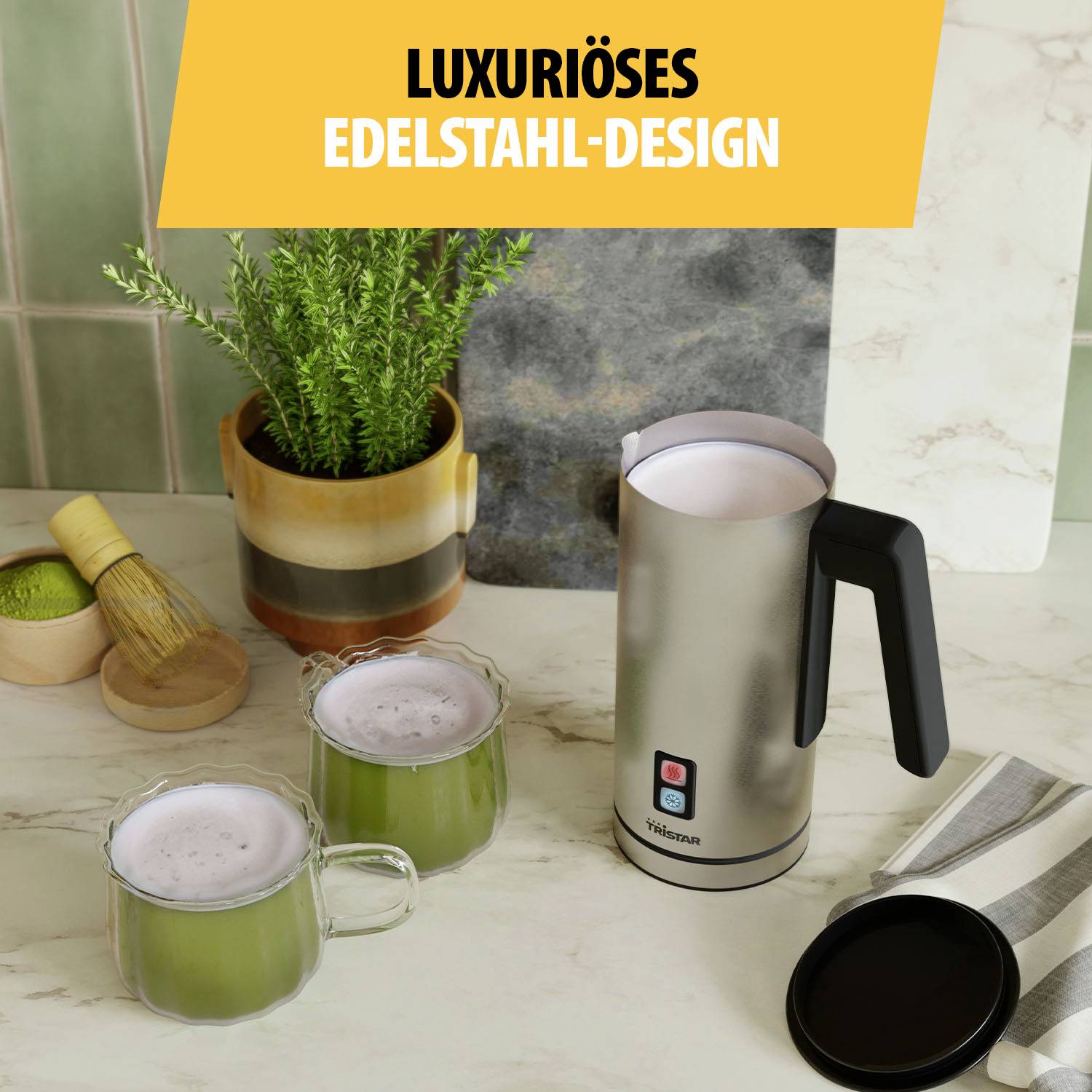 Silberner Wasserkocher auf Küchentisch mit zwei Tassen Matcha. Pflanze im Hintergrund. Text: Luxuriöses Edelstahl-Design.