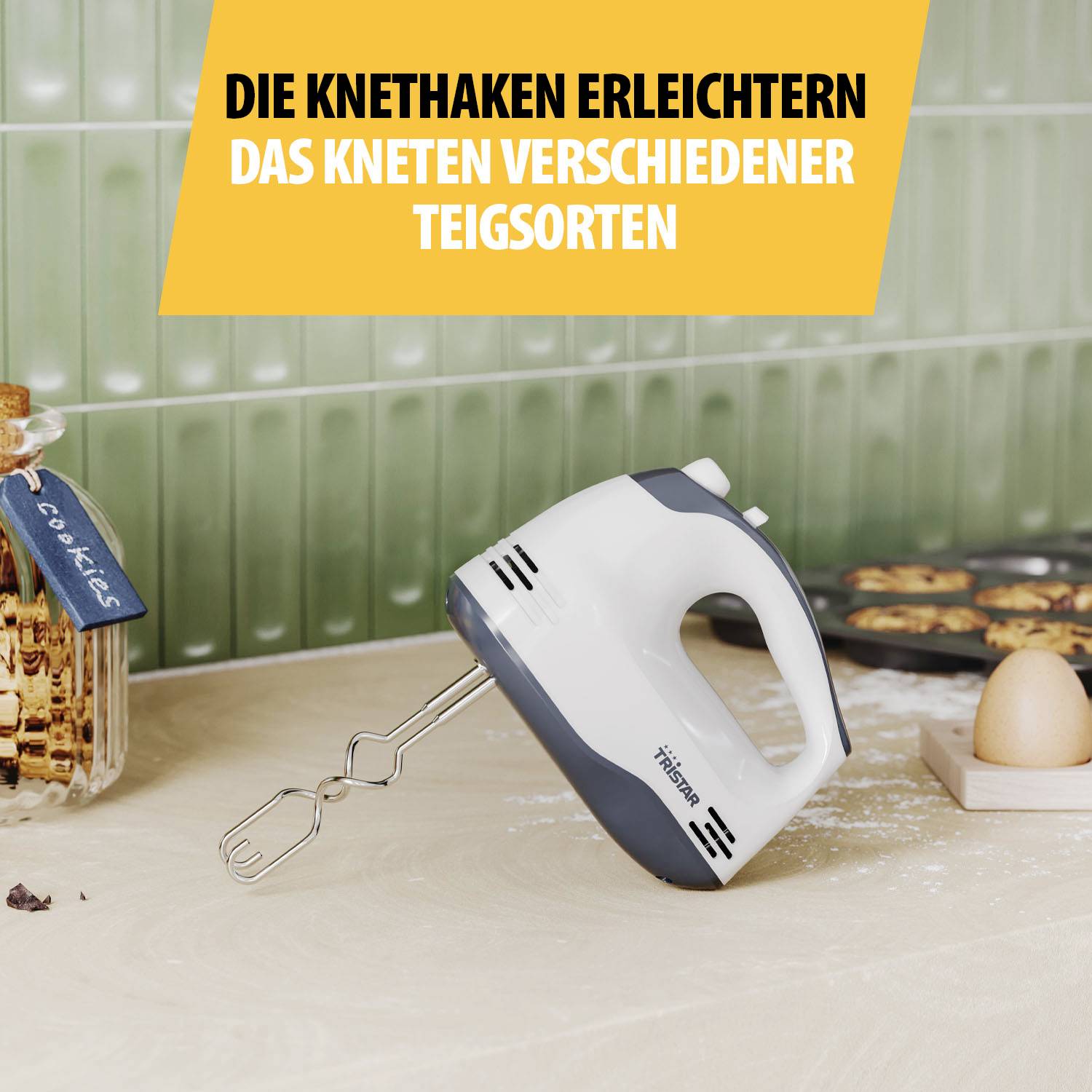 Ein Handmixer mit Knethaken steht auf einer Küchenarbeitsplatte. Im Hintergrund sind Plätzchen und eine Eierdose zu sehen.