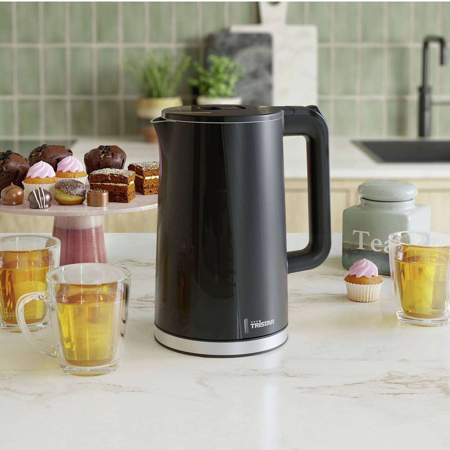 Ein schwarzer Wasserkocher steht auf einer Küchenarbeitsplatte, umgeben von Tee in Gläsern und einem Teller mit Donuts und Muffins.
