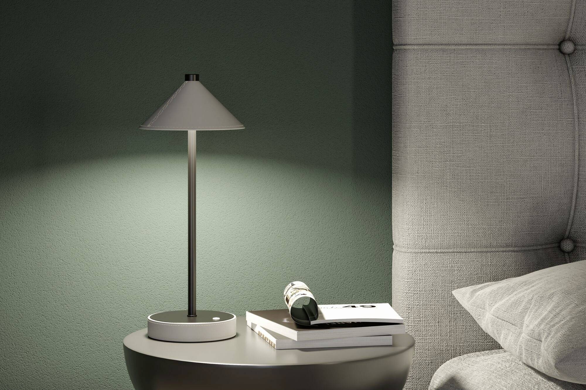 Nachttisch mit moderner Lampe, Büchern und gerolltem Magazin neben einem gepolsterten Kopfteil; sanft beleuchtete Ecke.