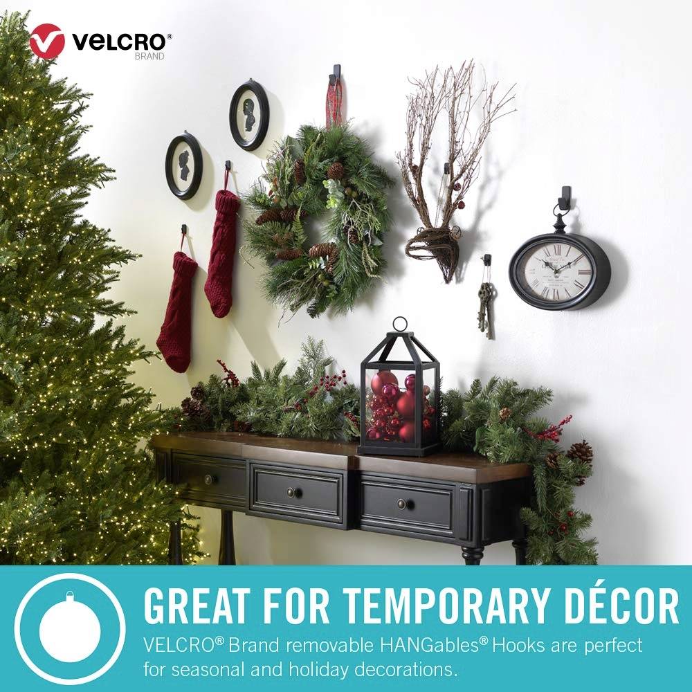 Wohnzimmer mit Weihnachtsdeko: Tannenbaum, Girlande, Kränze und Kerzen. Text betont VELCRO-Haken für saisonale Dekorationen.