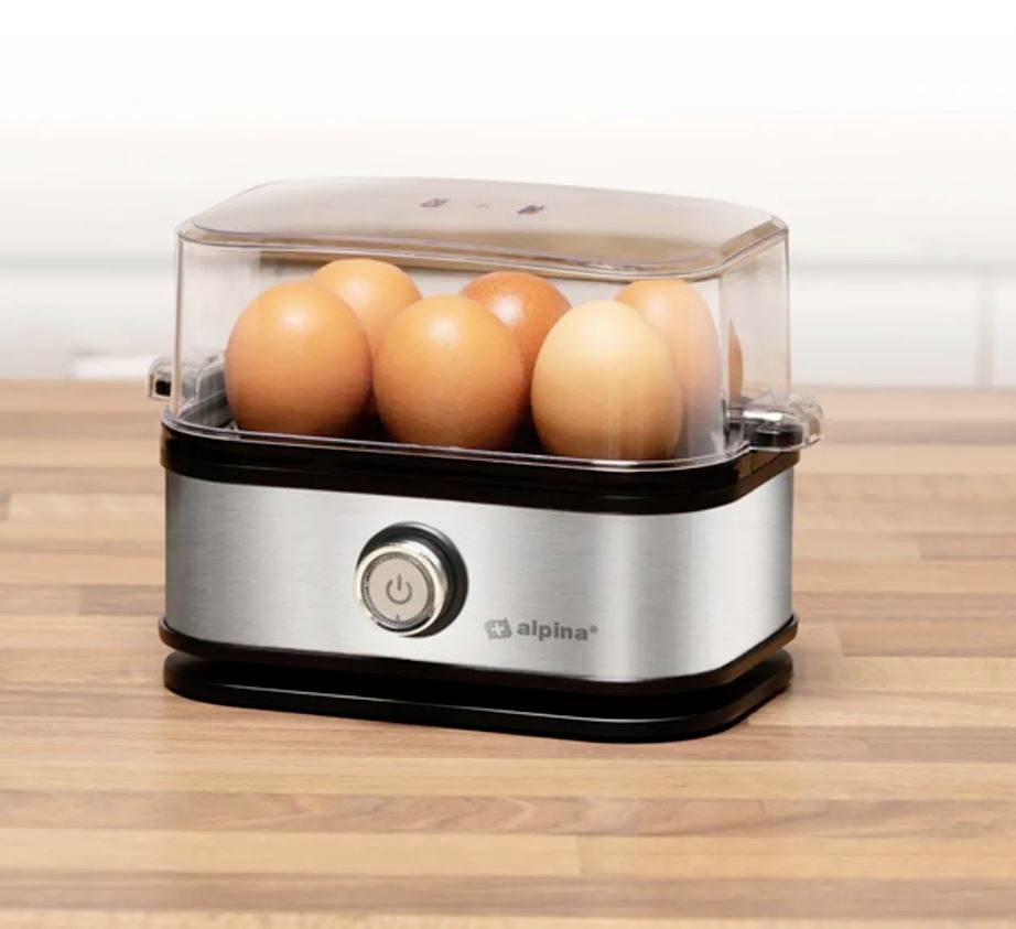 Ein elektrischer Eierkocher aus Edelstahl auf einer Holzoberfläche mit sechs braunen Eiern darin.