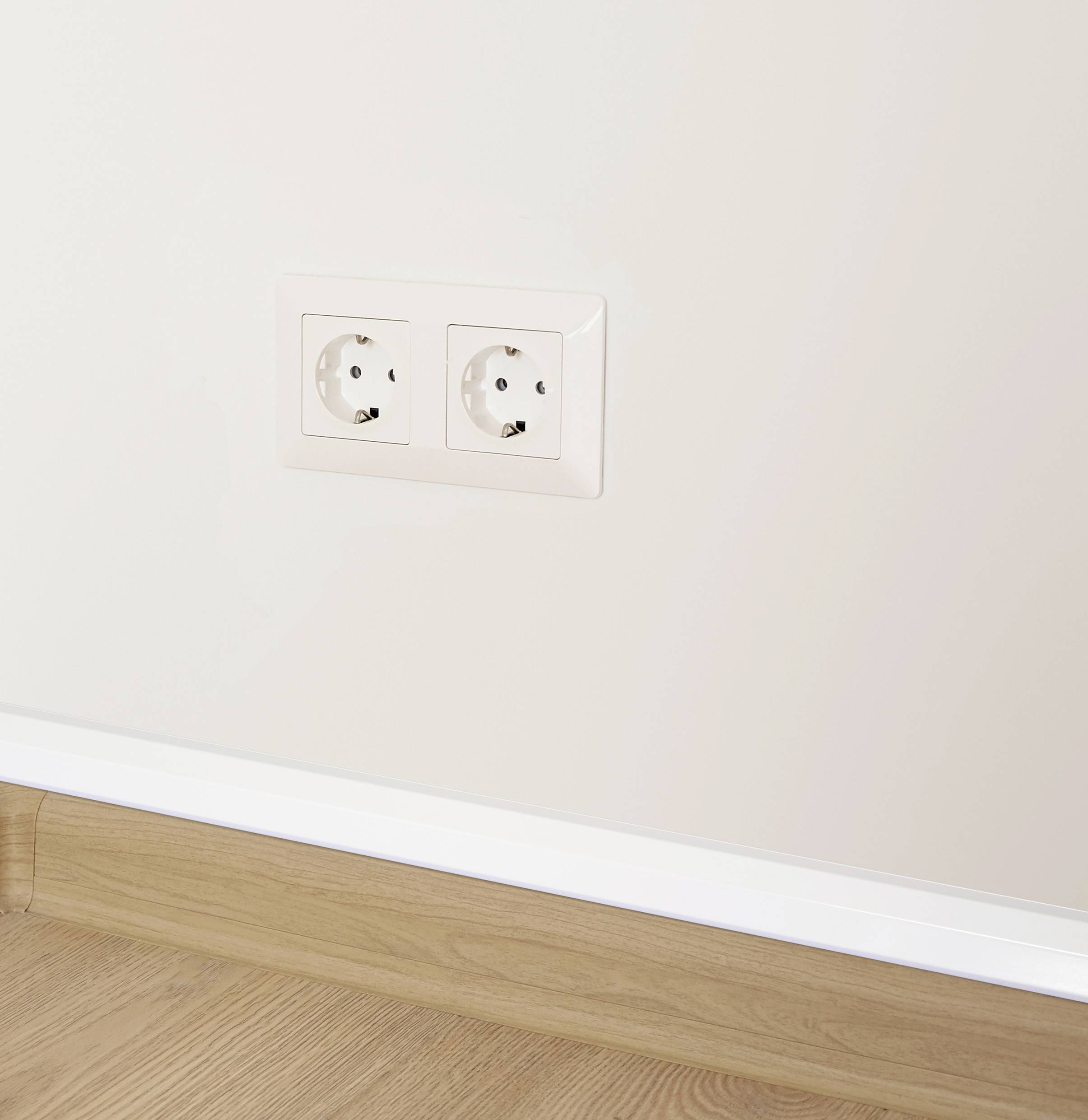 Zwei weiße Steckdosen in einer cremefarbenen Wand über einem Holzfußboden.