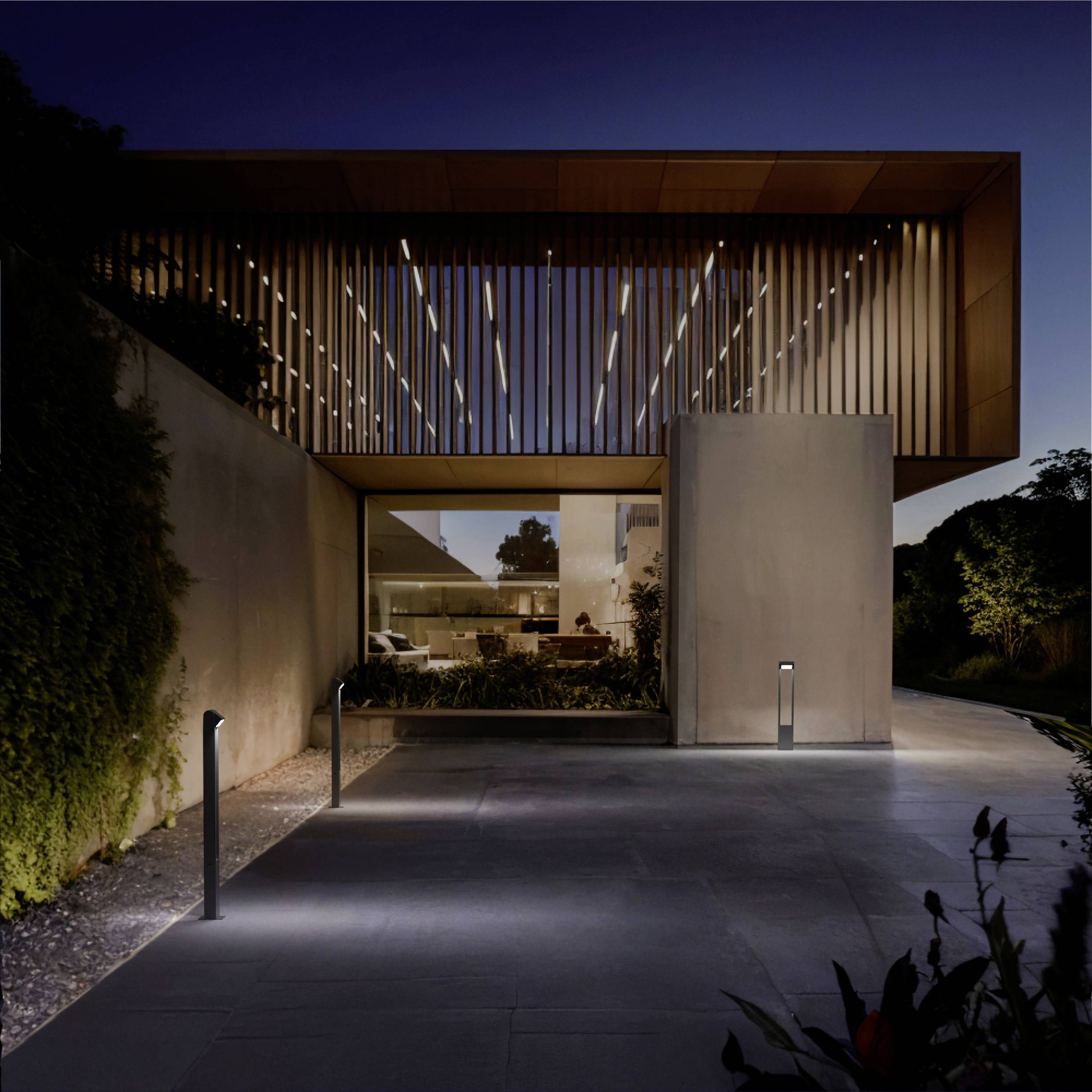 Ein modernes Haus in der Abenddämmerung mit Holzlamellen-Design und warmem Licht, umgeben von Grünpflanzen. Minimalistische Architektur mit großen Fenstern.