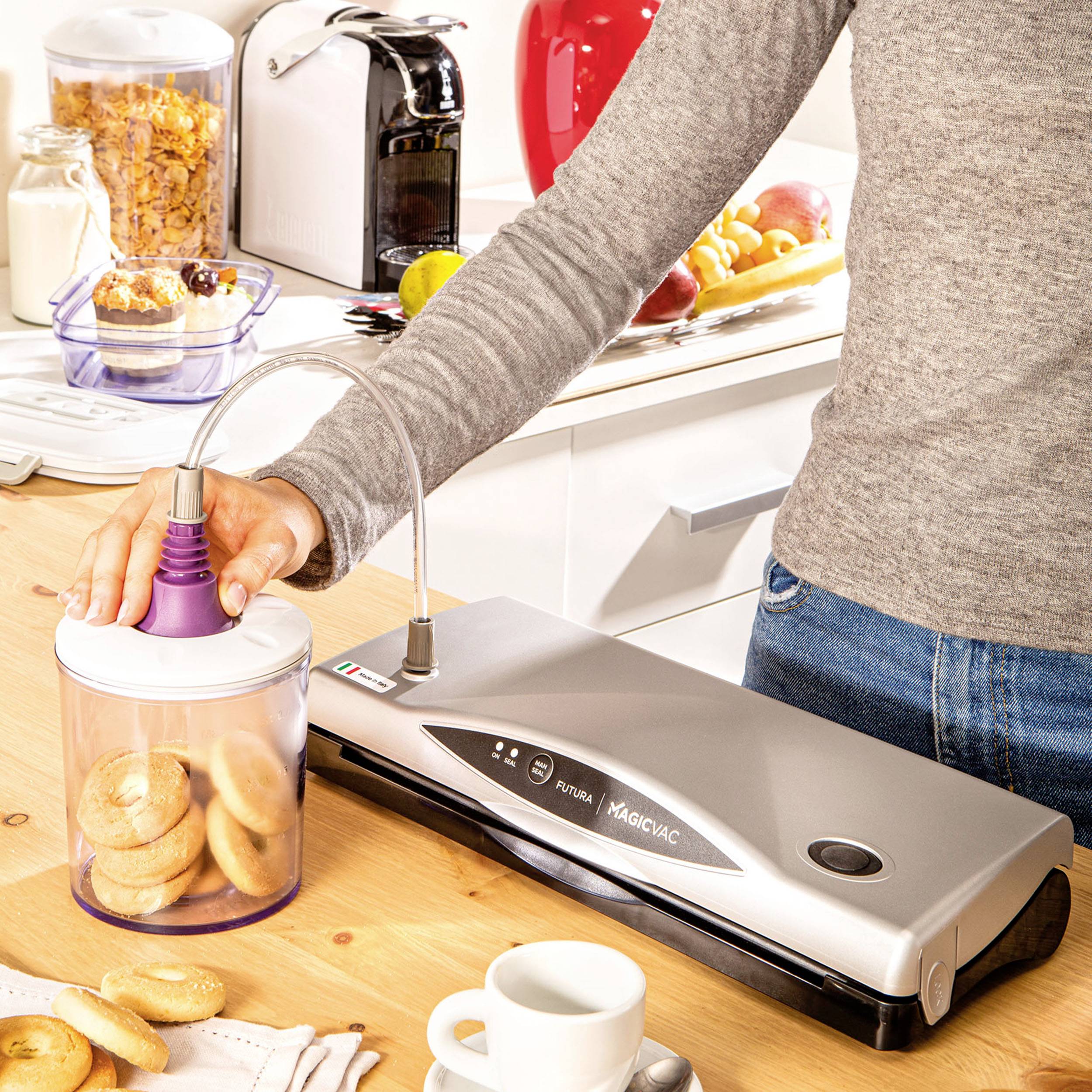 Eine Person verschließt einen Beutel mit Gebäck mithilfe eines Vakuumiergeräts auf einer Küchentheke. Haushaltsgegenstände im Hintergrund.