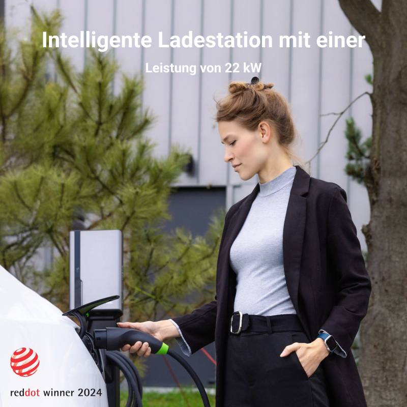 Eine Frau lädt ein Elektrofahrzeug an einer intelligenten Ladestation mit 22 kW Leistung. Im Hintergrund sind Pflanzen sichtbar.